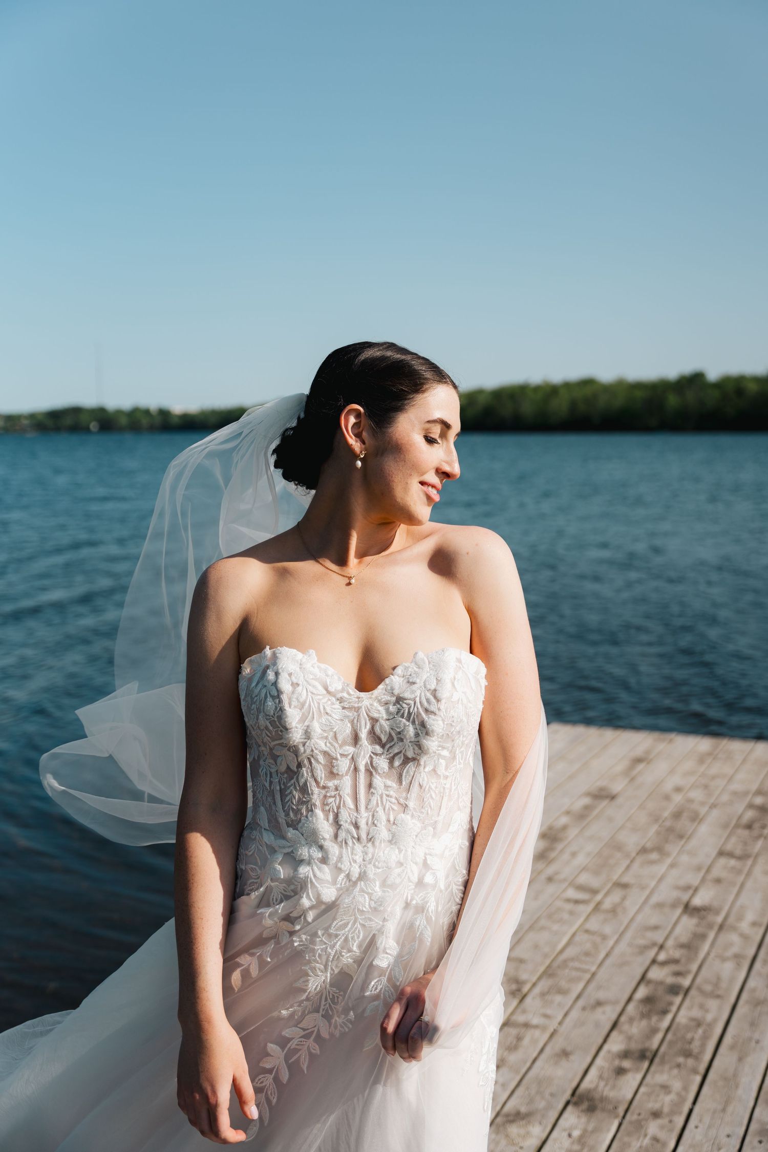 A white lace wedding dress with sweetheart neckline photographed on a wooden dock by a lake in Halifax, Nova Scotia.