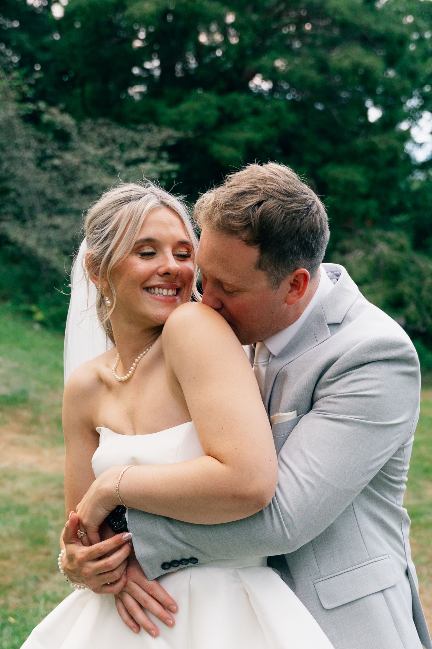 Romantic wedding couple embracing outdoors surrounded by lush greenery in Halifax, Nova Scotia.