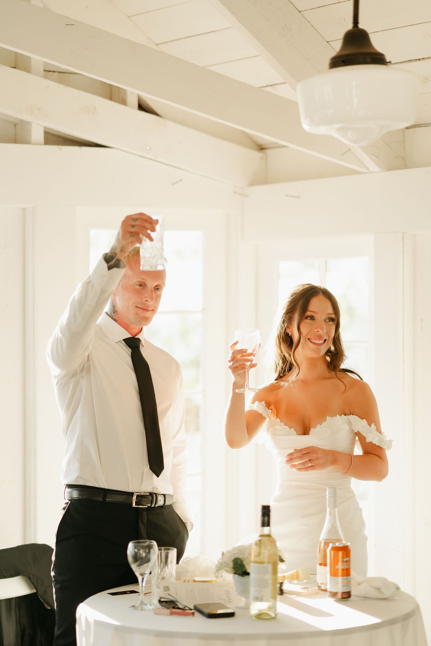 Wedding guests raise glasses in a toast during a bright, sunlit reception in an all-white venue in Halifax, Nova Scotia.