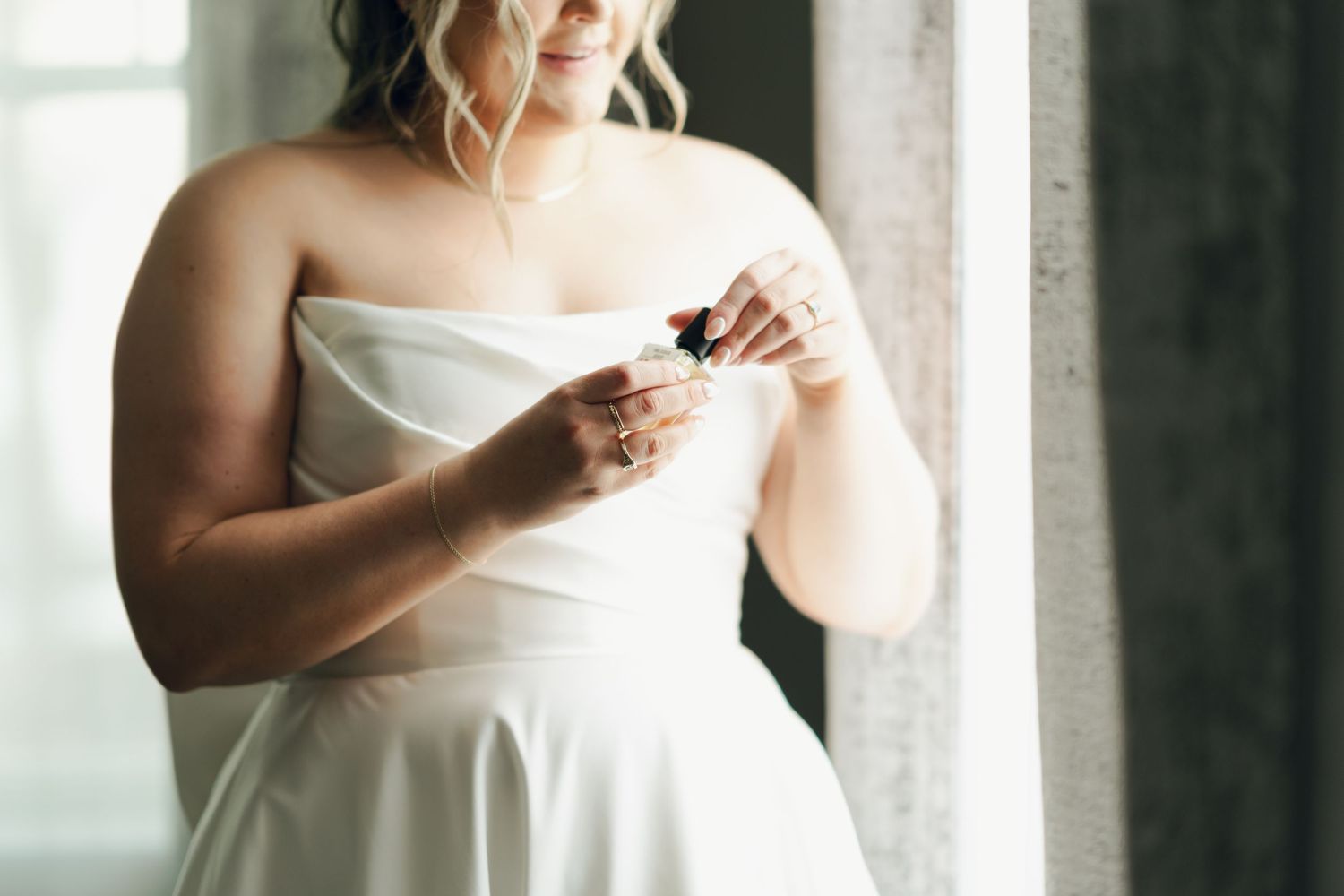 Bride in white dress holds bouquet while standing near window in soft natural light in Halifax, Nova Scotia.