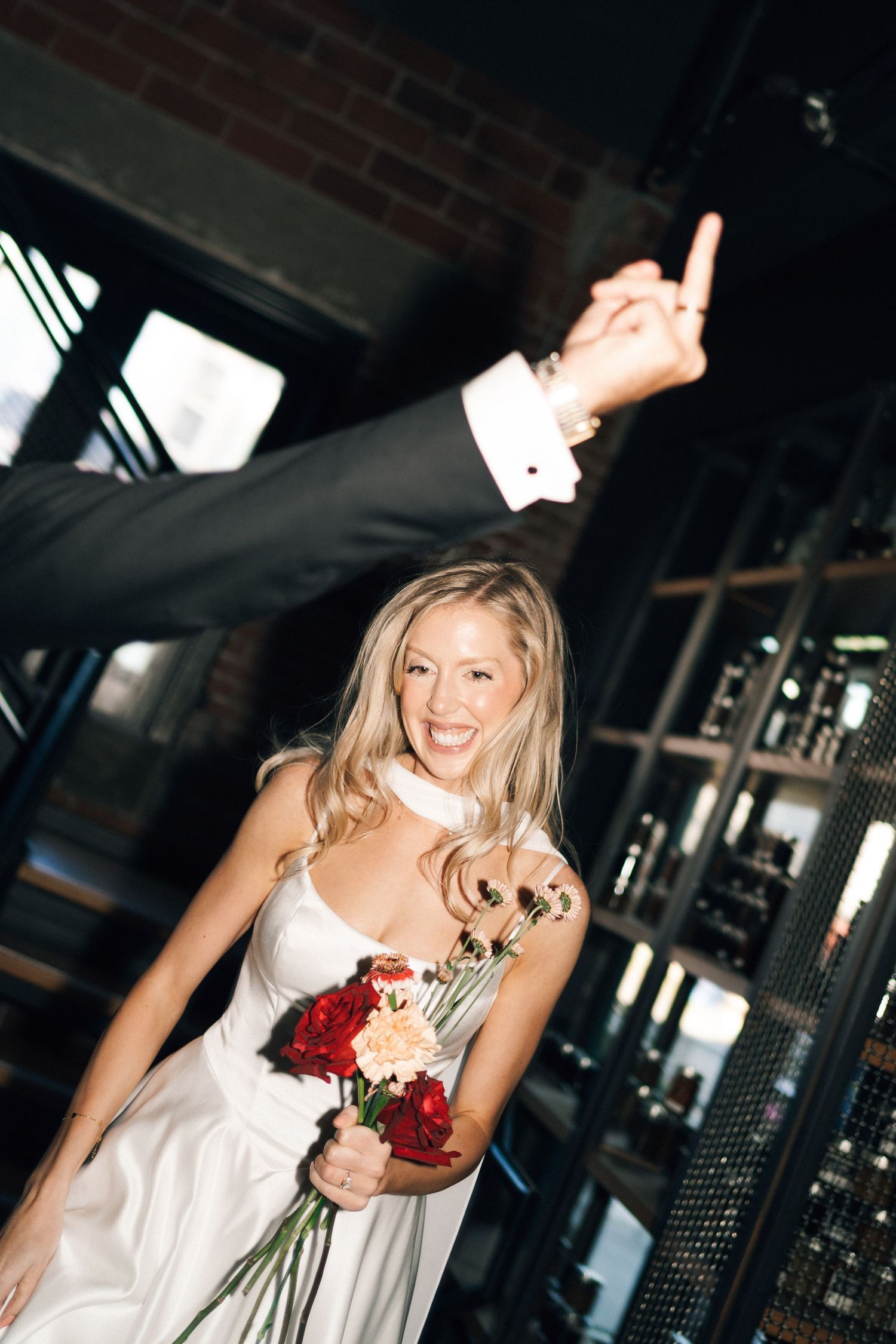 A bride in a white dress holds red flowers while dancing and celebrating at an indoor venue in Halifax, Nova Scotia.