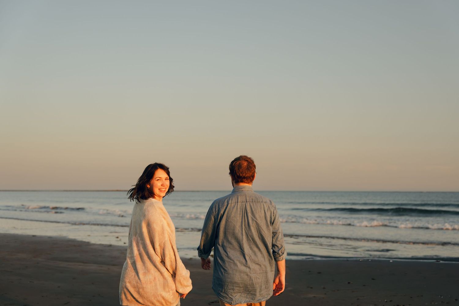 Two people walking together on a serene beach in Halifax, Nova Scotia at sunset with ocean waves in the background.