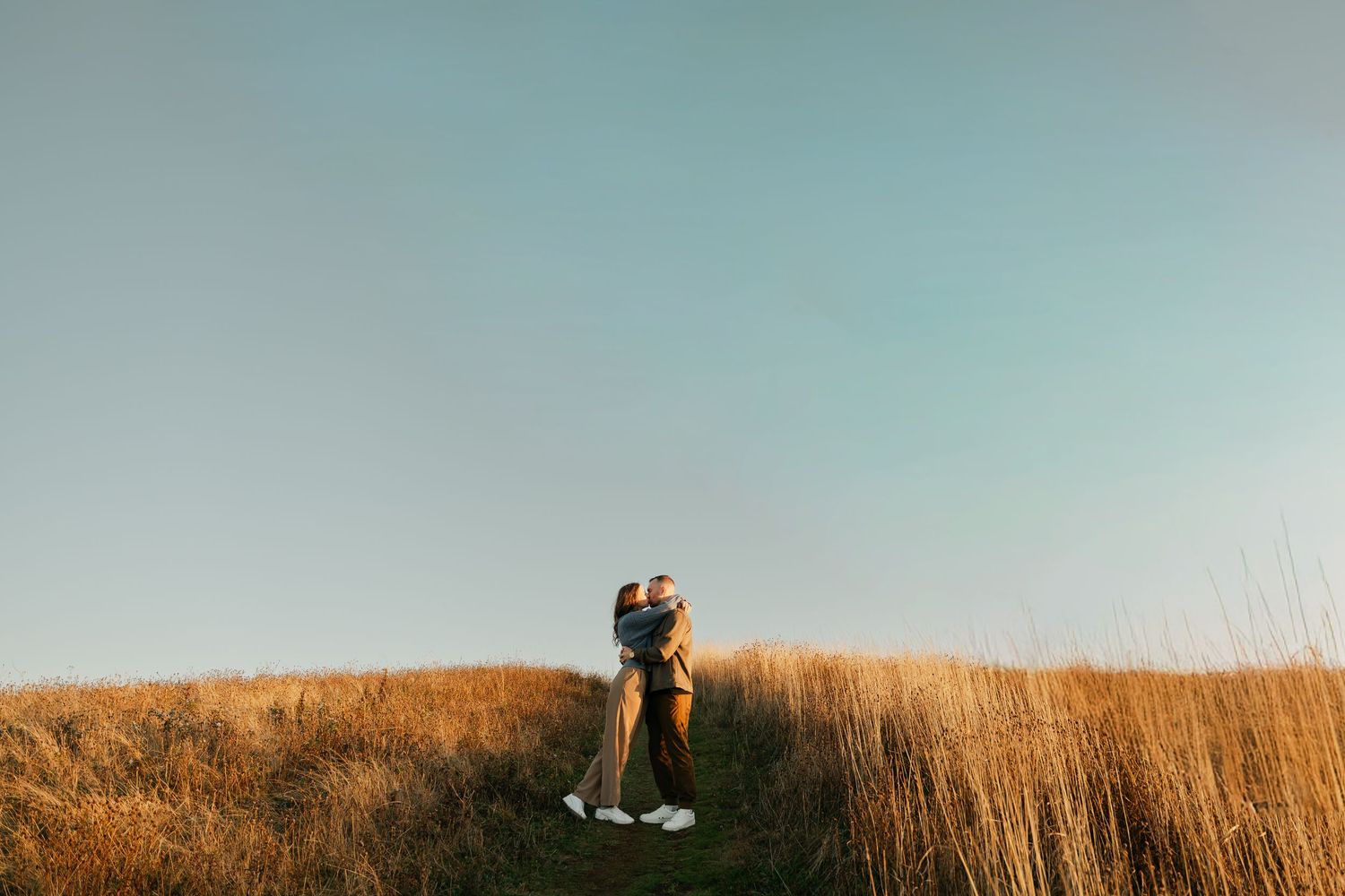 Couple embraces in golden wheat field during sunset with warm light illuminating the tall grass in Halifax, Nova Scotia.