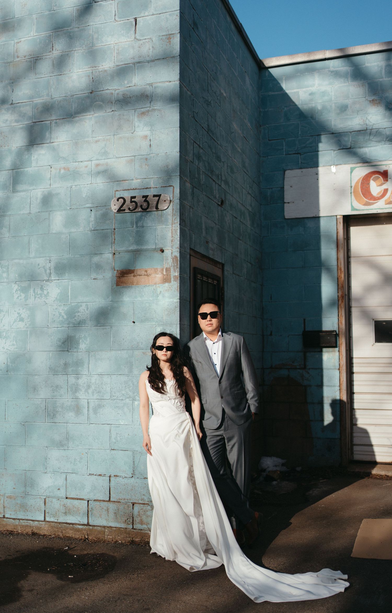 A couple in wedding attire poses against a light blue wall with shadows creating dramatic angles in Halifax, Nova Scotia.
