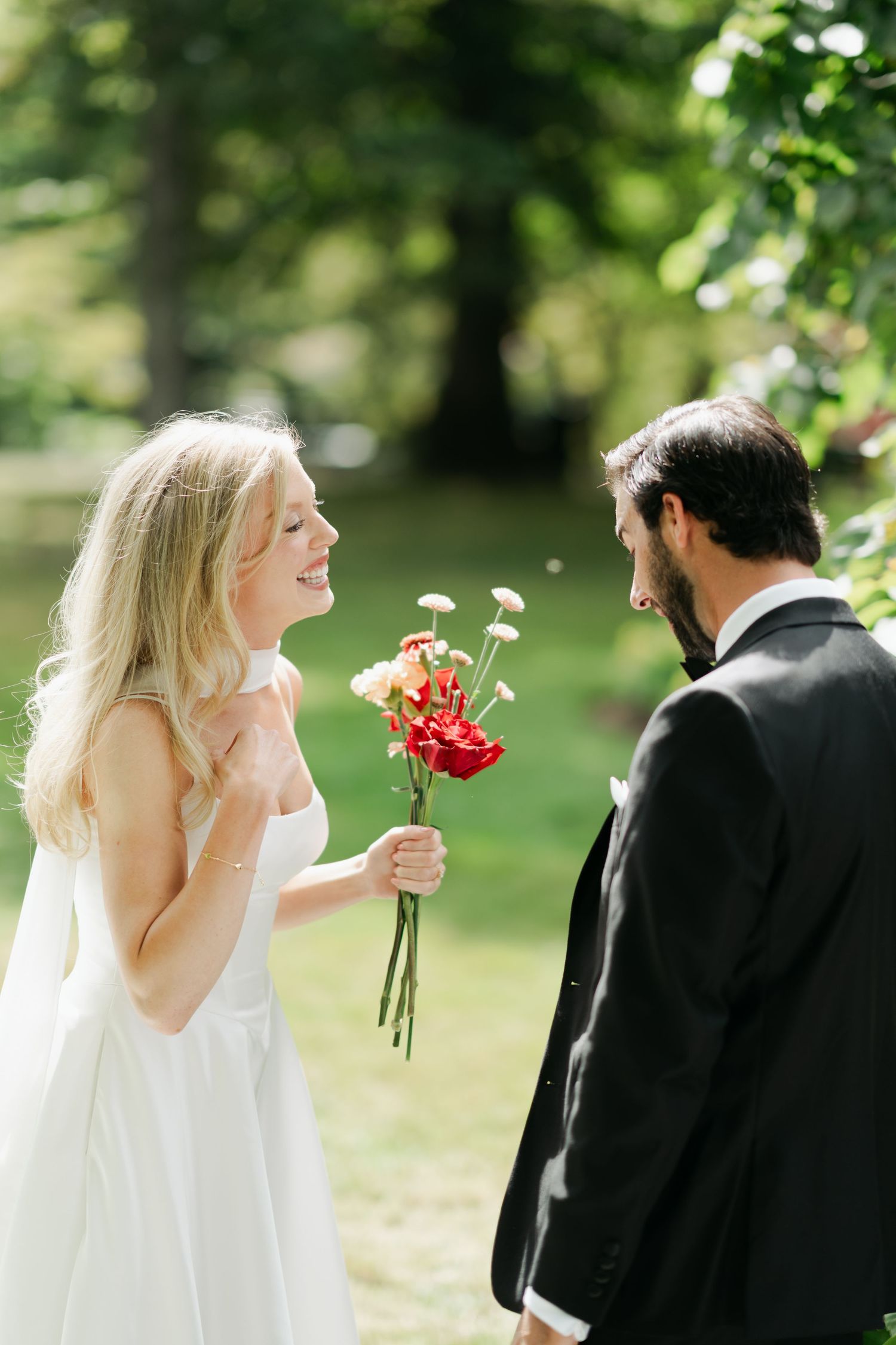A romantic wedding moment captured in a sunlit garden with red flowers in Halifax, Nova Scotia.