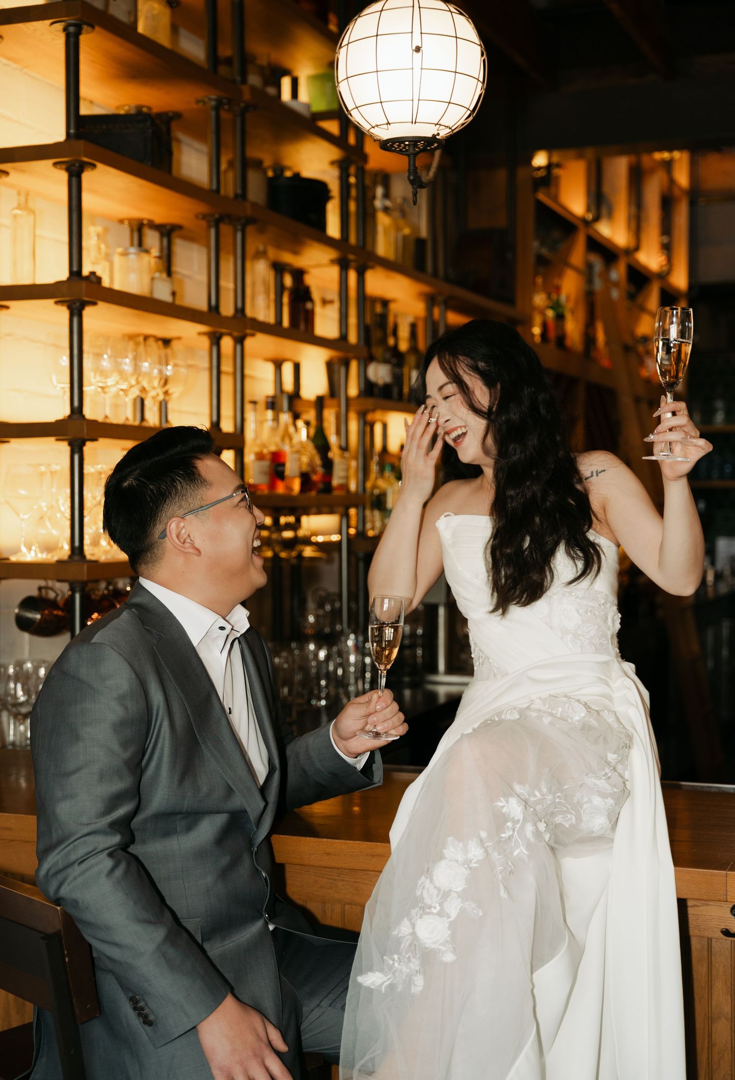 A couple shares a joyful moment at a bar with a white paper lantern and illuminated bottle display in the background in Halifax, Nova Scotia