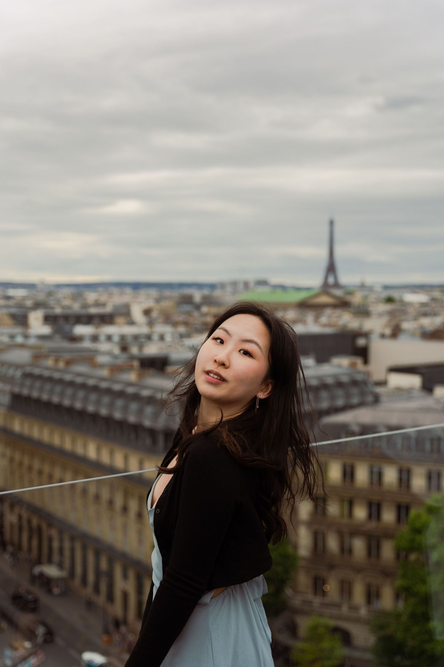 A scenic view of Paris rooftops and the Eiffel Tower in the distance on an overcast day.