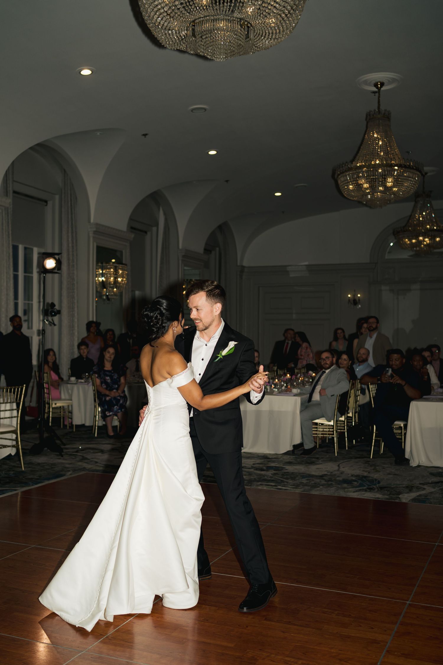 A couple shares their first dance at a wedding reception under elegant crystal chandeliers in an arched ballroom in Halifax, Nova Scotia.