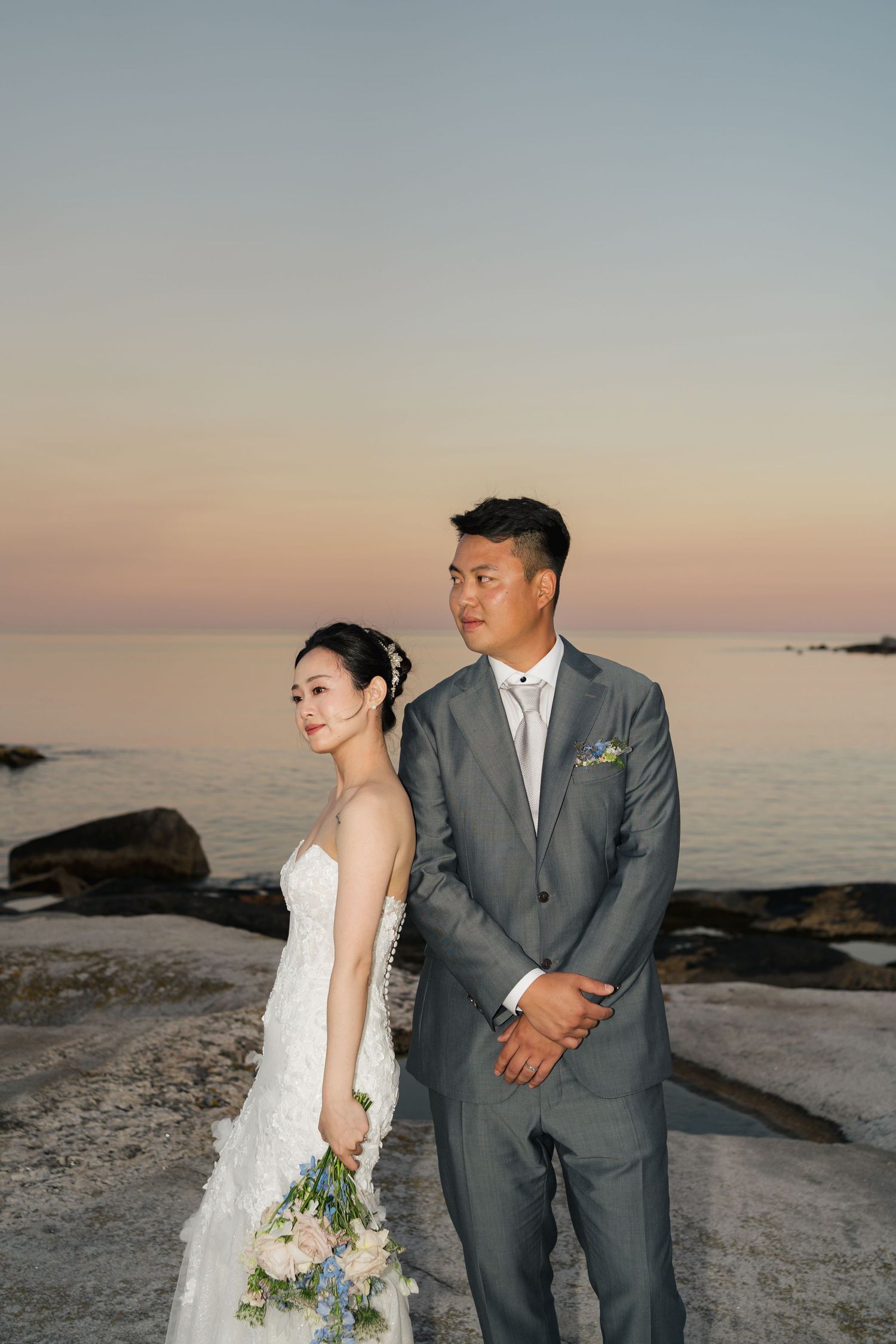 Couple in wedding attire posing at sunset on a rocky beach coastline in Halifax, Nova Scotia.