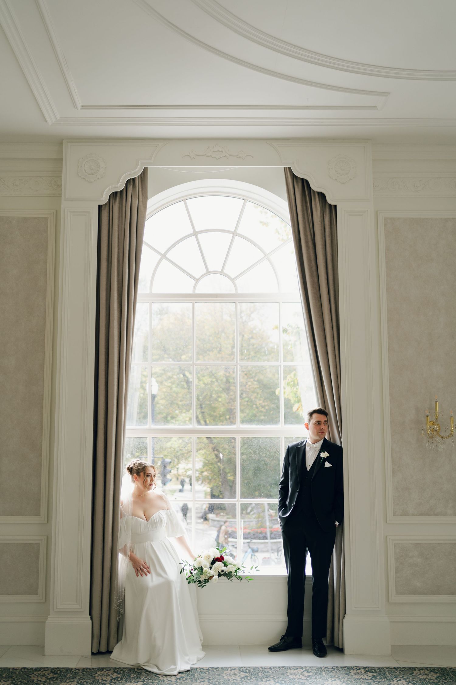 Elegant white room with arched windows serves as backdrop for formal wedding portraits at Lord Nelson Hotel, Halifax, Nova Scotia.