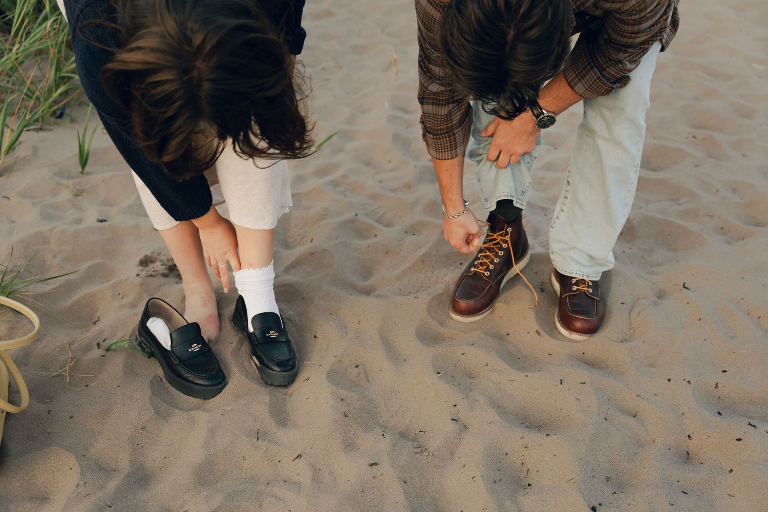 A candid moment of a couple's collection of shoes and feet standing on sandy beach terrain in Halifax, Nova Scotia.