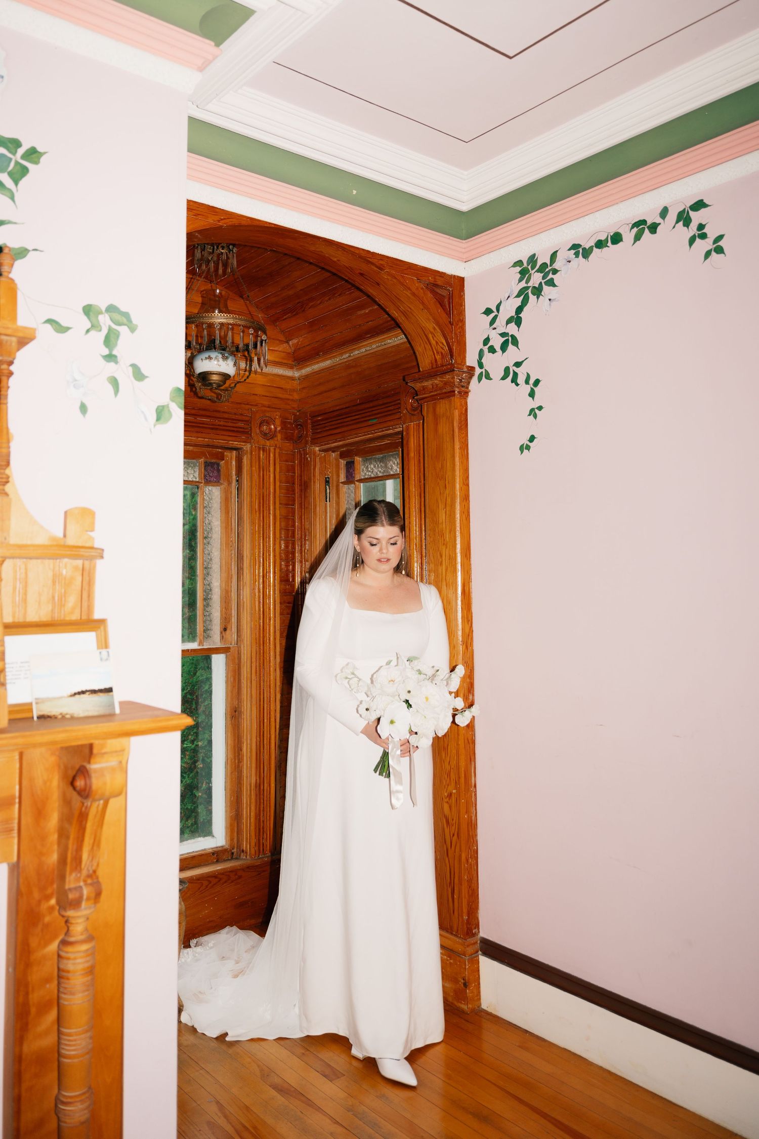 Bridal portrait white walls with green trim and decorative ivy border meet warm wooden doorways in an elegant interior hallway.