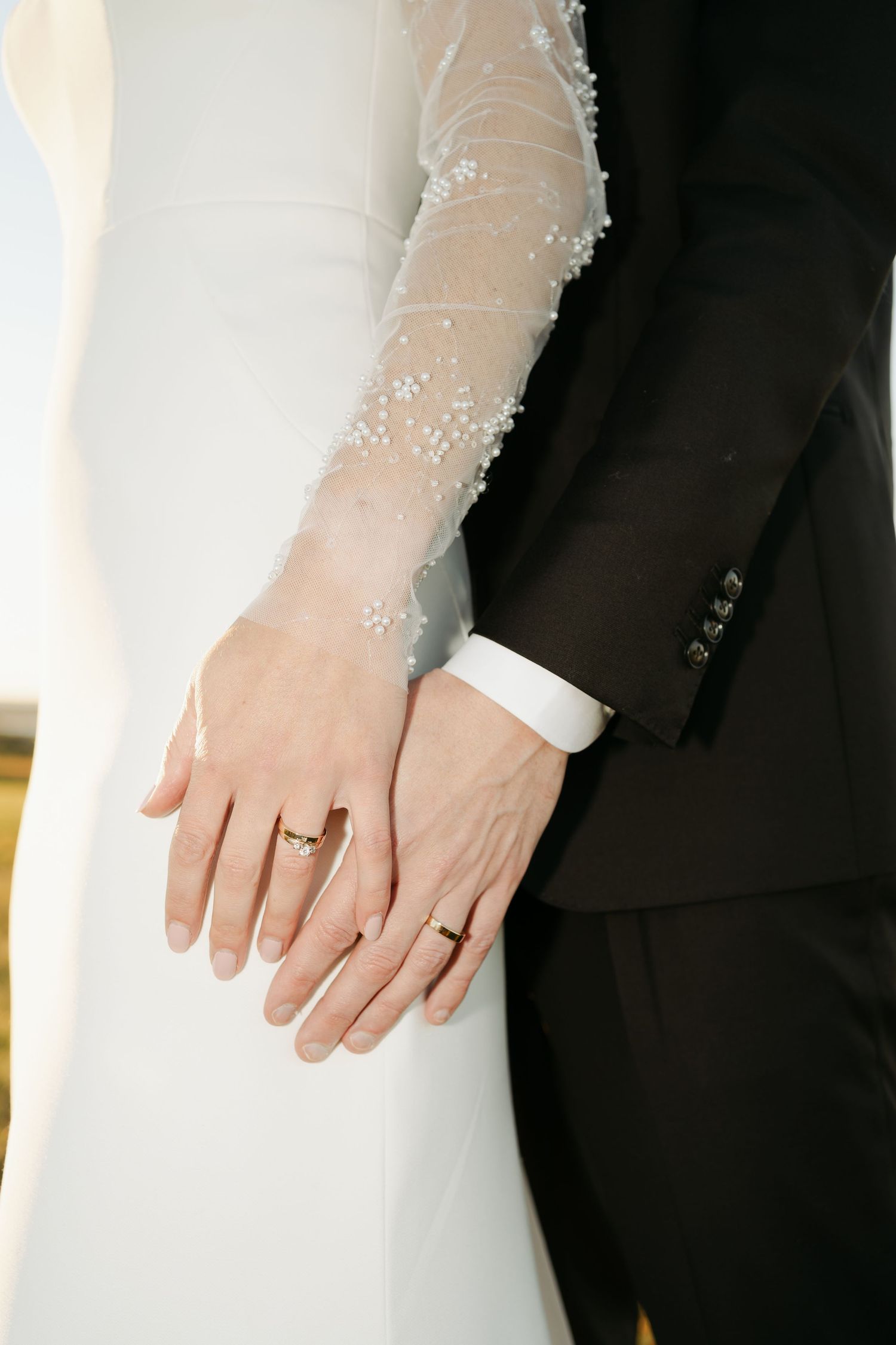 Close-up details of wedding rings and delicate lace on formal attire in natural lighting.