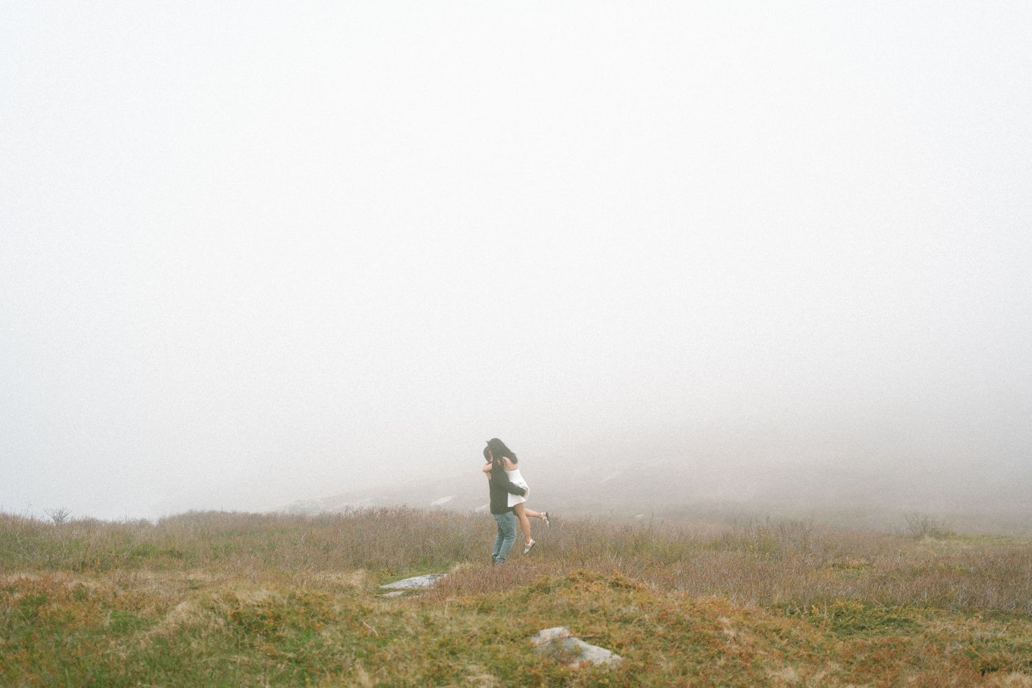 A foggy mountain landscape with a person hiking through the misty terrain and tall grass in Halifax, Nova Scotia.