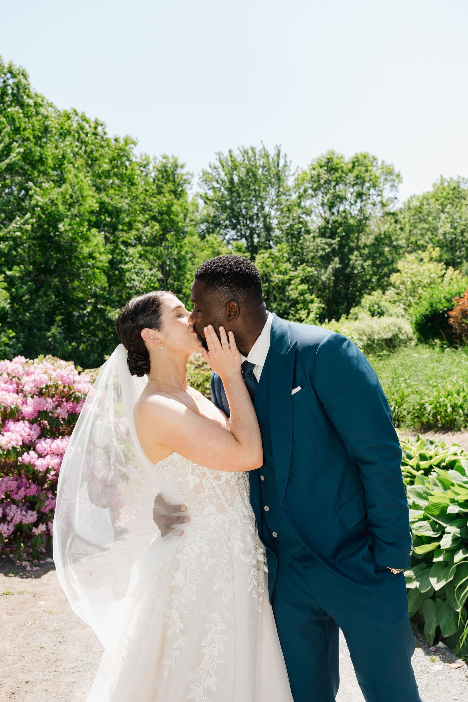 A joyful wedding couple shares an intimate moment in a garden with blooming flowers and lush greenery in Halifax, Nova Scotia.