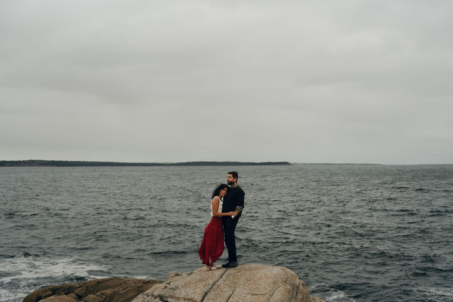 People sitting on rocky coastline in Halifax, Nova Scotia overlooking misty ocean waves and mountains in the distance.