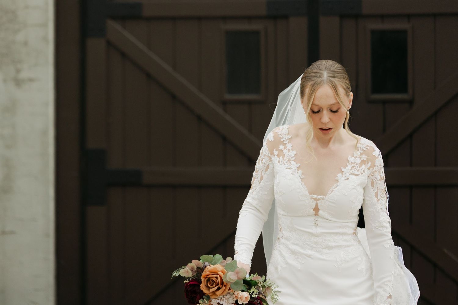 A bride in an elegant lace wedding dress stands in a rustic setting with soft natural lighting at Lightfoot & Wolfville.