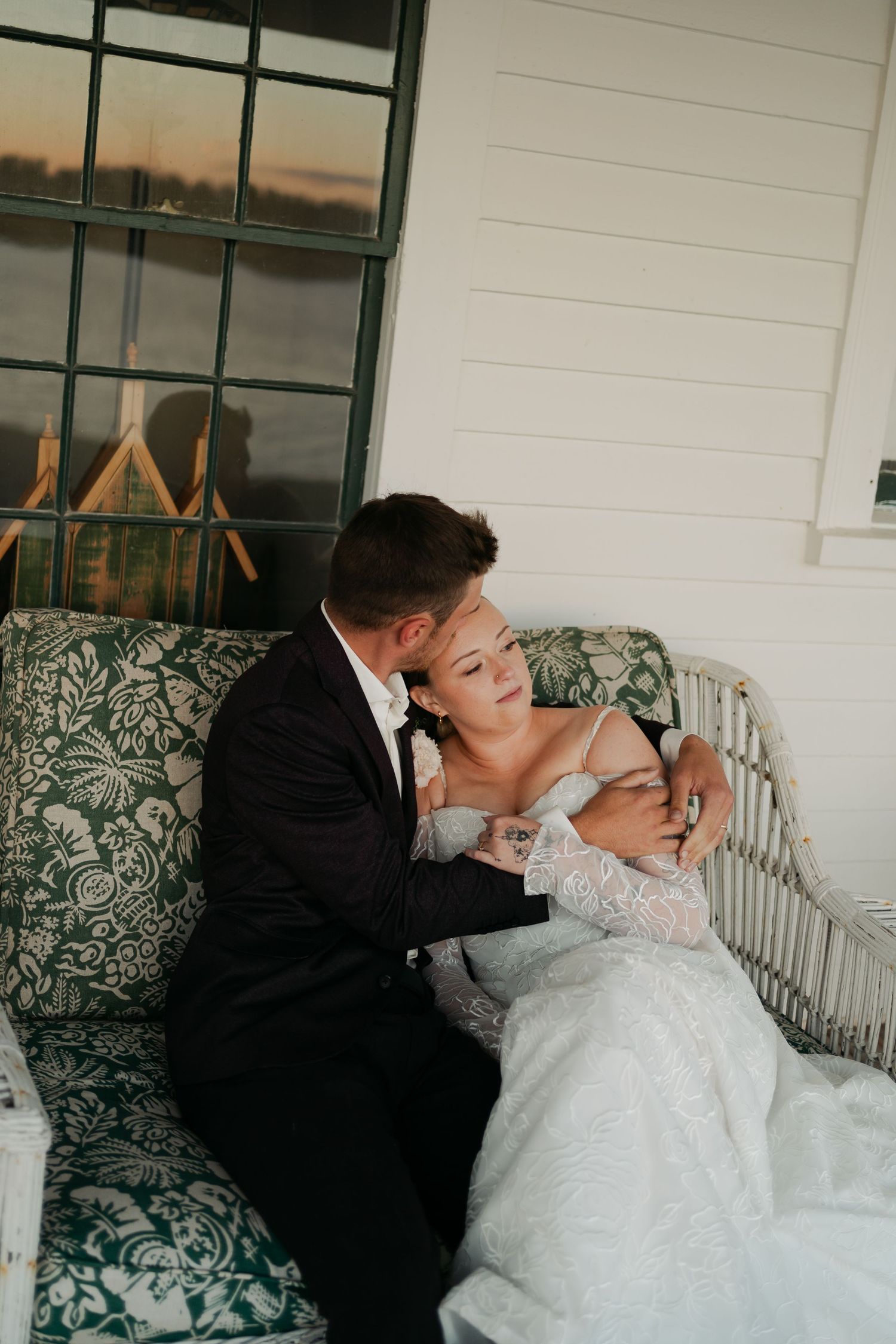 Romantic wedding couple shares intimate moments on a white porch swing with green floral cushions in Nova Scotia.