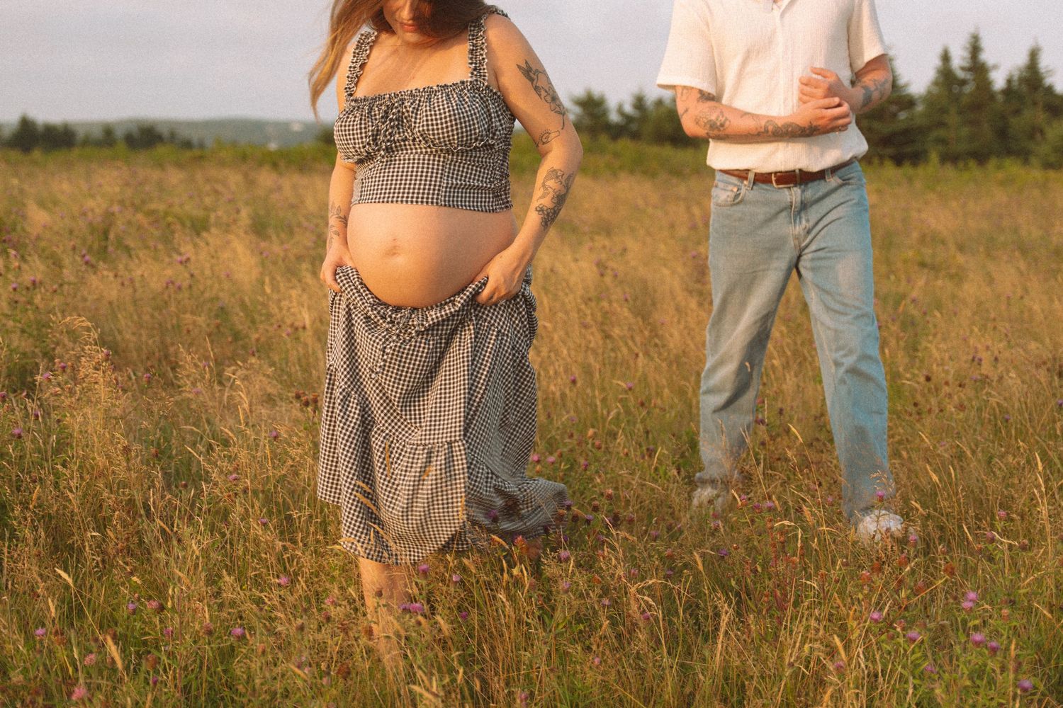 A couple walking through a golden field at sunset with long shadows cast across the grass in Lawrencetown, Halifax, Nova Scotia.