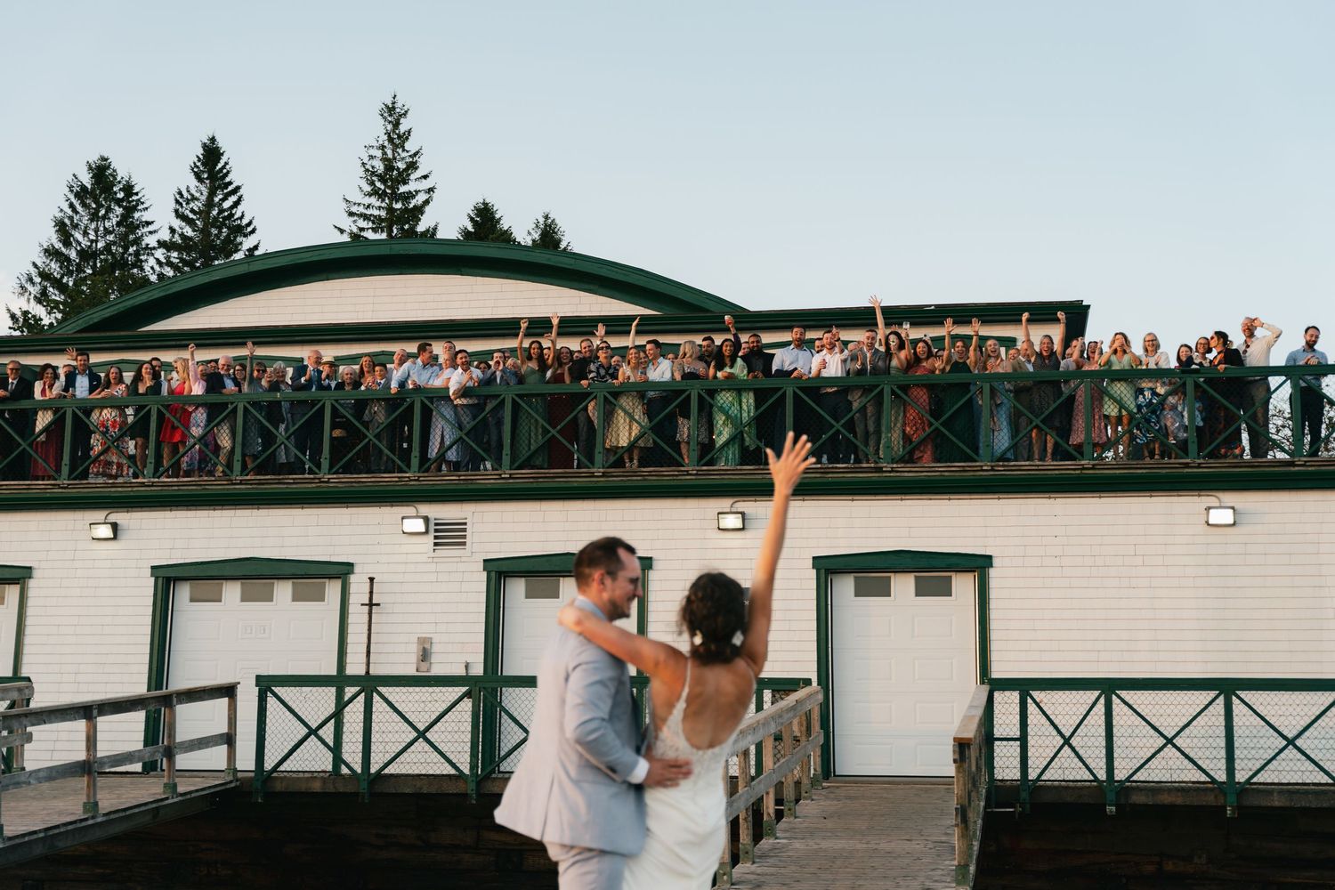 Wedding guests cheer from a balcony deck overlooking an outdoor venue during a celebration in Halifax, Nova Scotia.