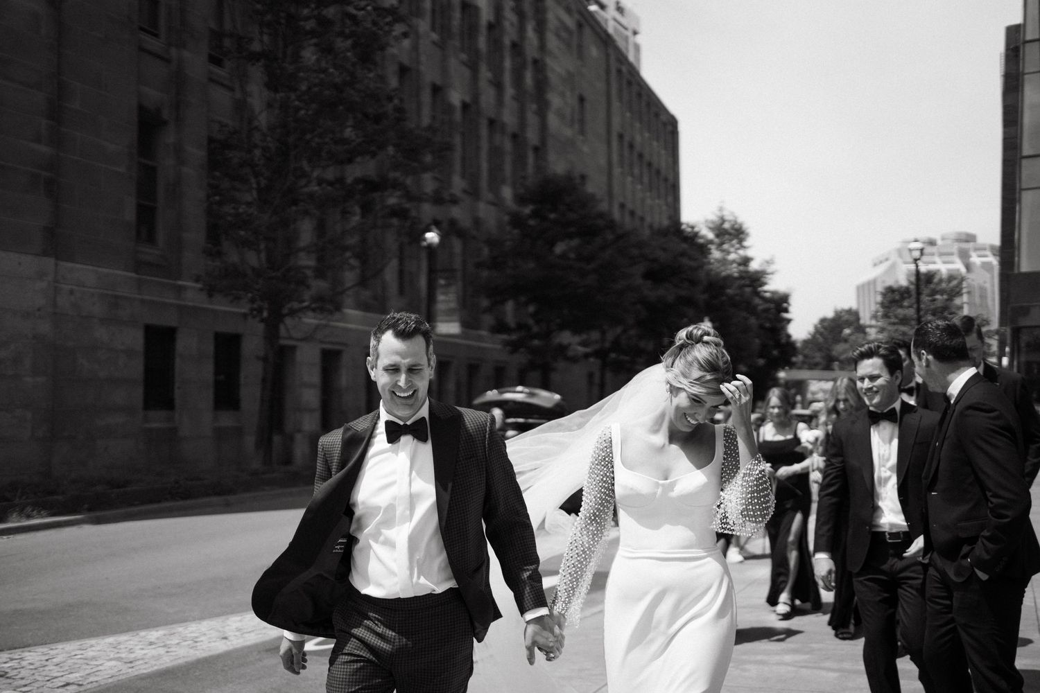 A wedding party walks along an urban street with tall buildings in black and white in Halifax, Nova Scotia.