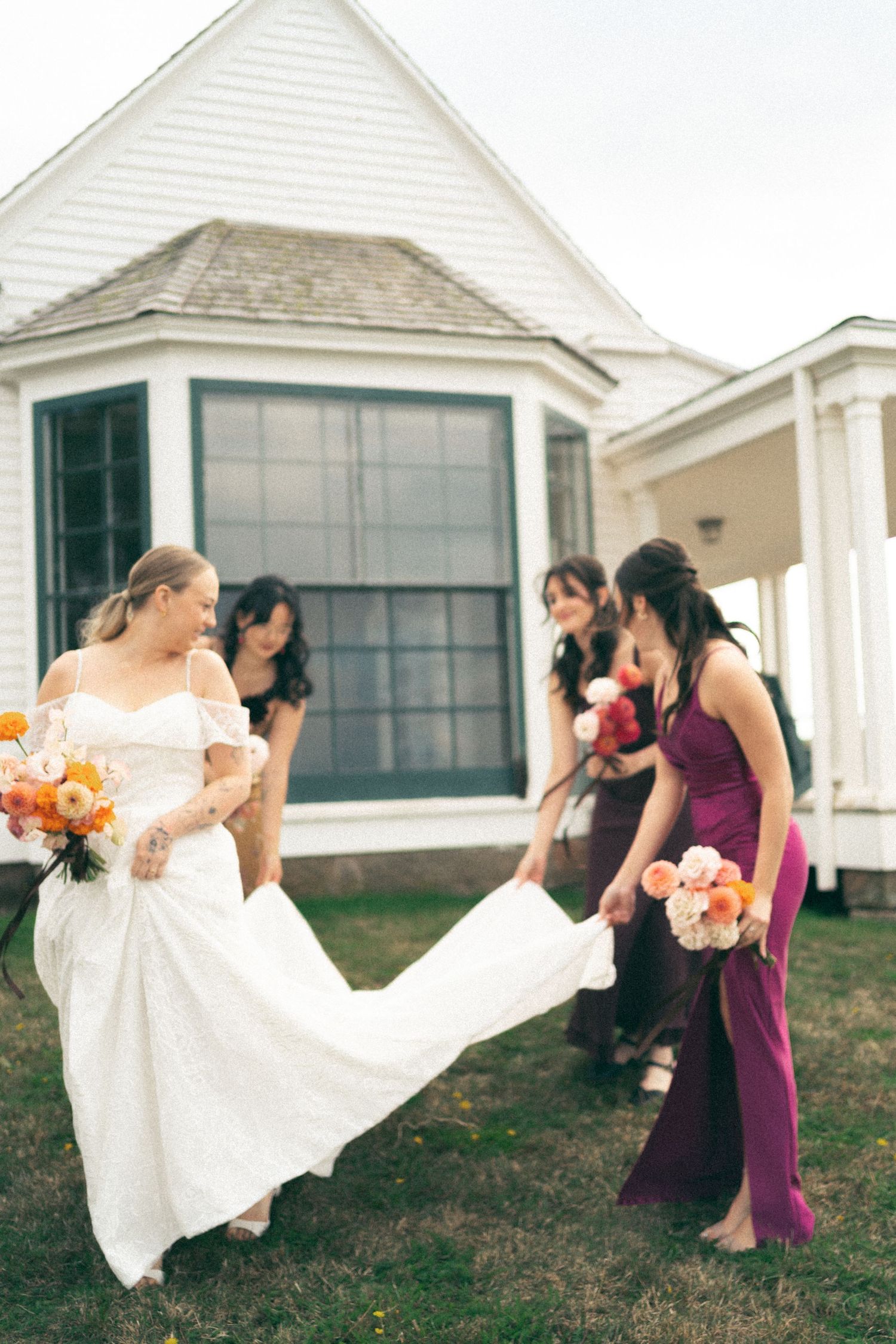 Wedding party in purple dresses and white gown posing in front of white coastal cottages in Nova Scotia.