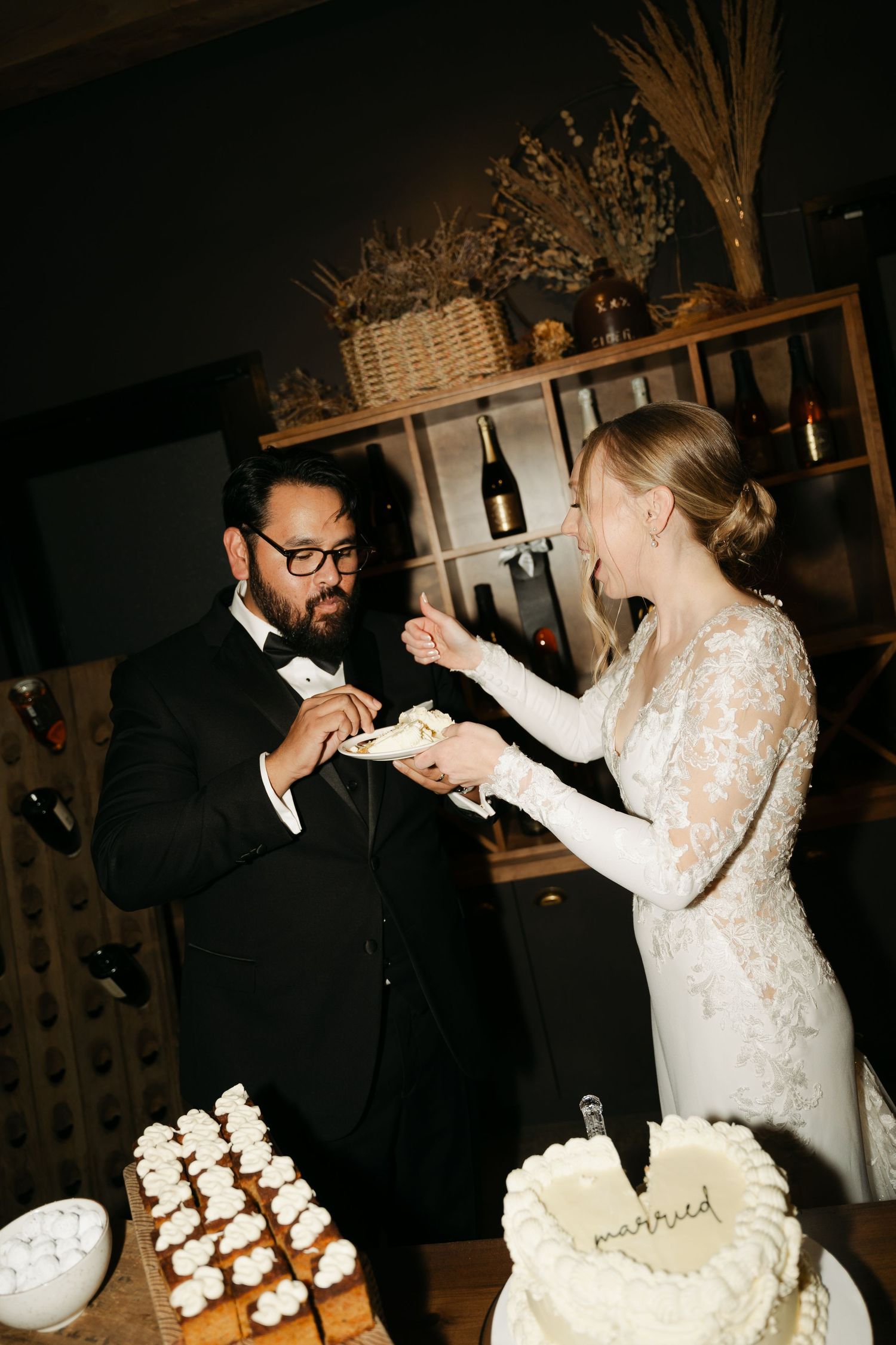 A wedding couple shares a playful moment while cutting their wedding cake and cupcake tower in a dimly lit reception at Lightfoot&Wolfville.
