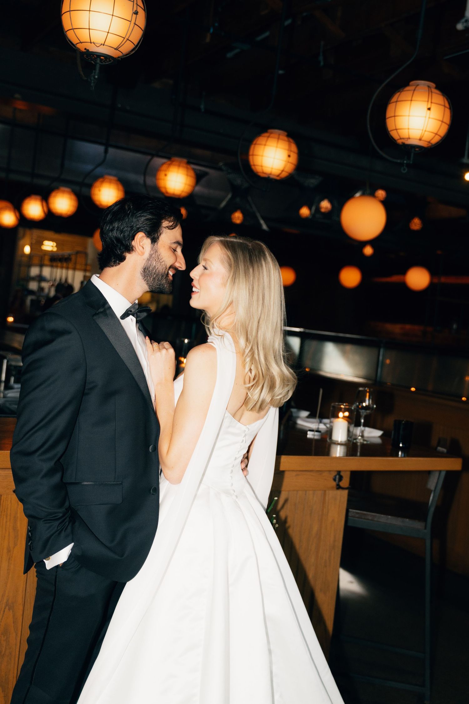 A romantic wedding moment under glowing orange paper lanterns in a dimly lit restaurant setting at Agricola Street Brasserie in Halifax.