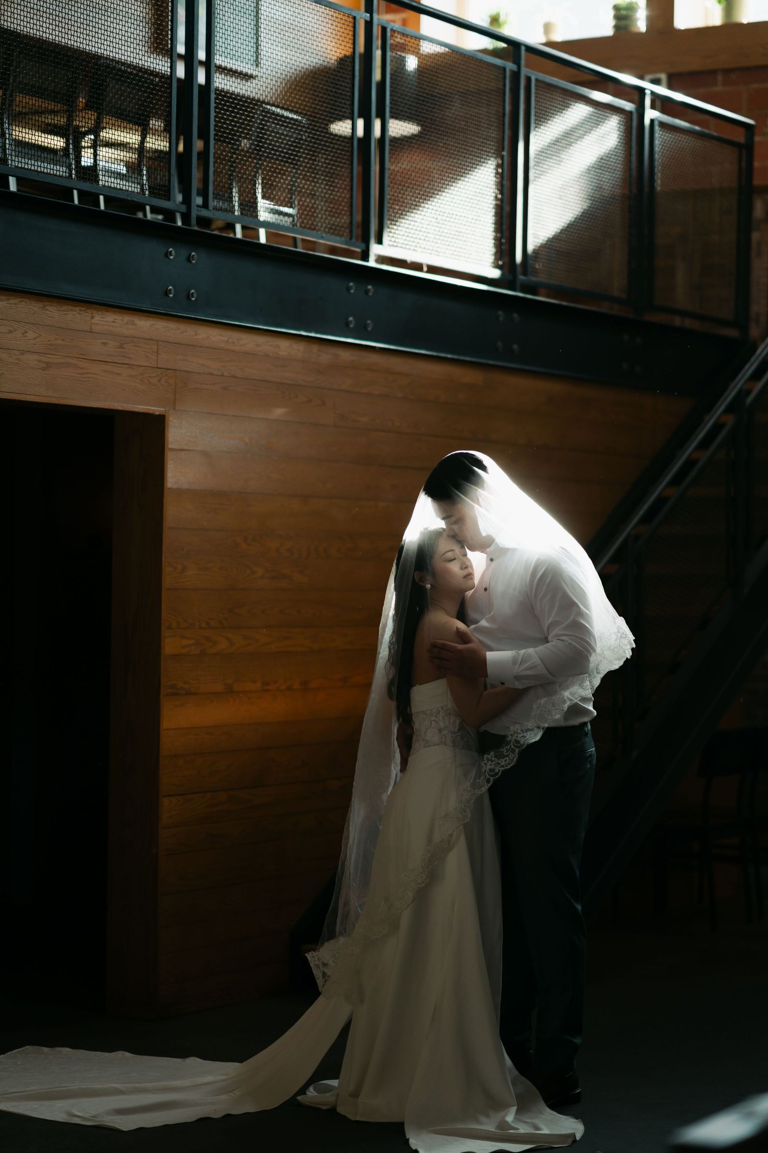A romantic wedding couple shares an intimate moment in a dimly lit industrial venue with wooden walls in Halifax, Nova Scotia.