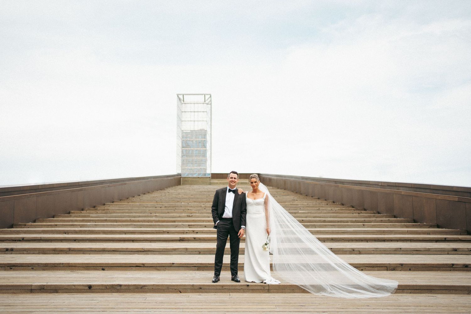 A couple in wedding attire stands at the bottom of a grand staircase leading to a tall white monument in Halifax, Nova Scotia.