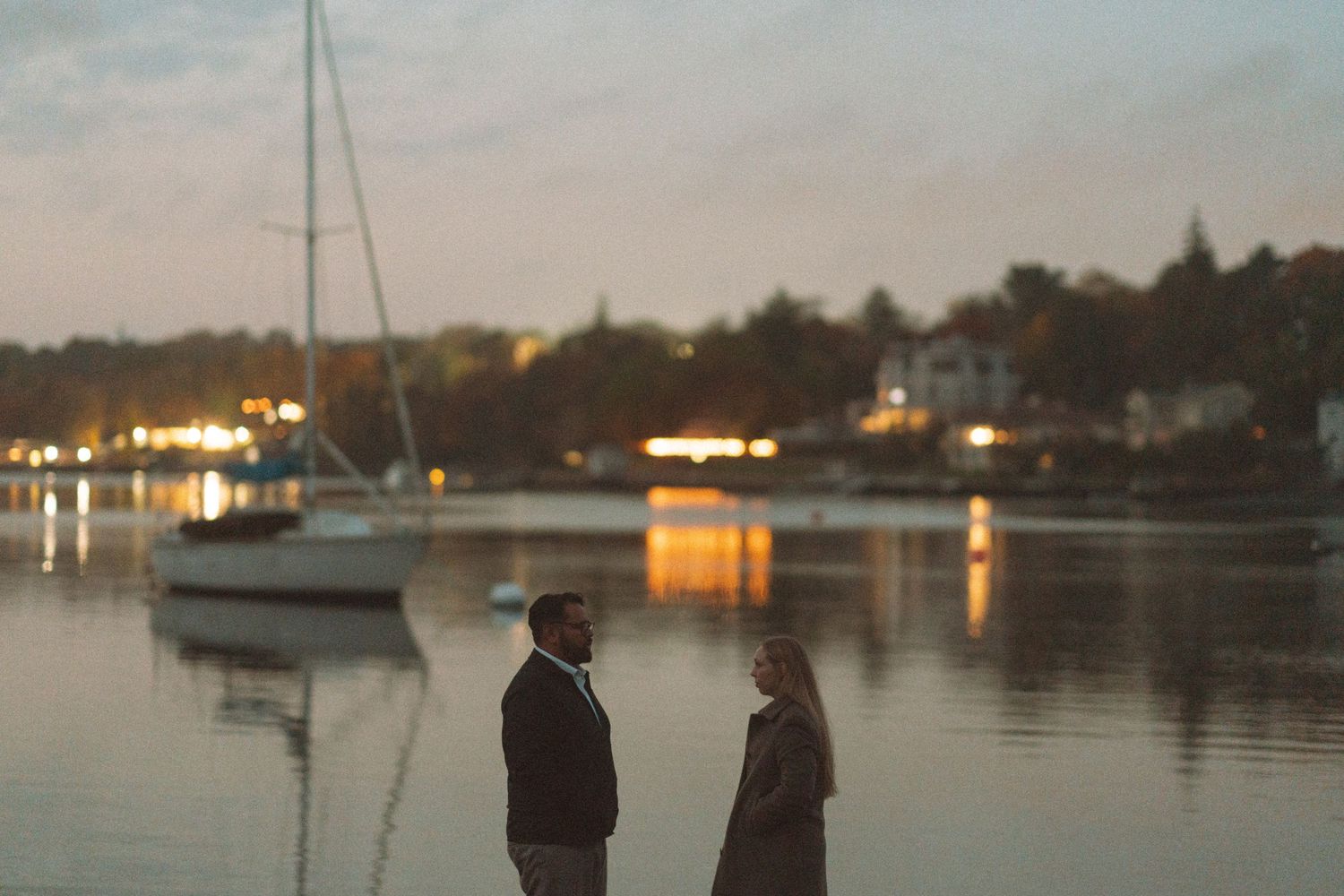A sailboat anchored in a calm harbor at dusk with twinkling lights reflecting on the water in Halifax, Nova Scotia.