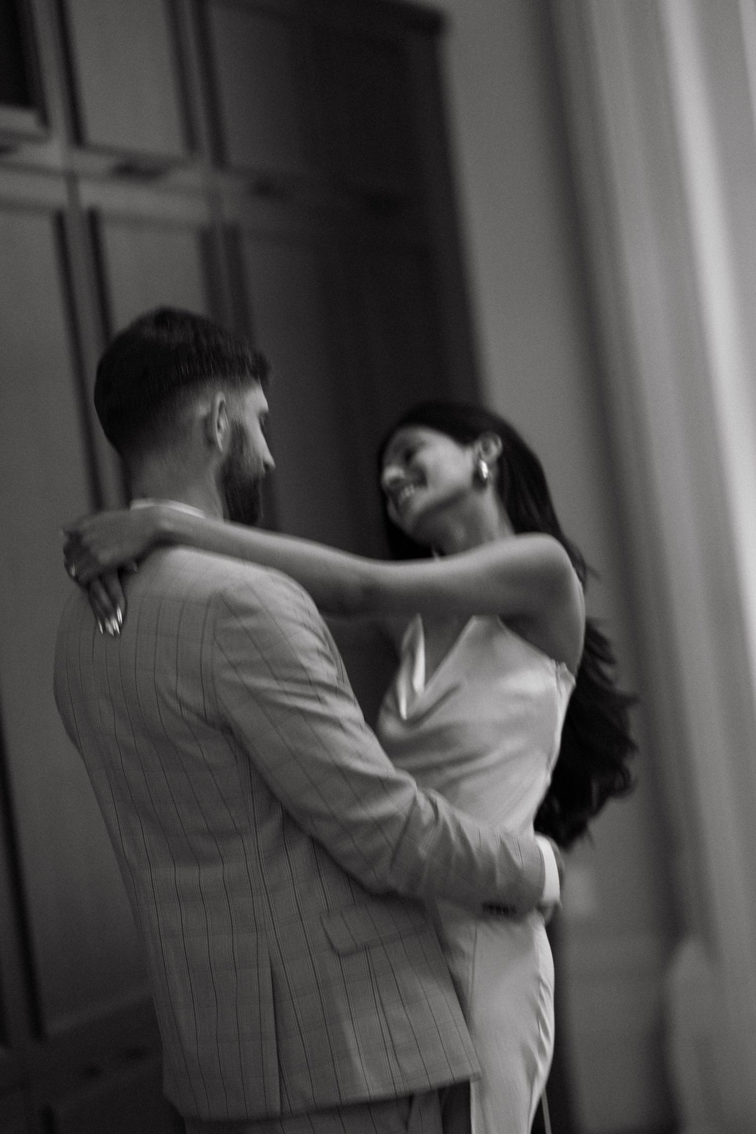 A romantic black and white photo of a couple embracing in an intimate dance pose near a window in Halifax, Nova Scotia.
