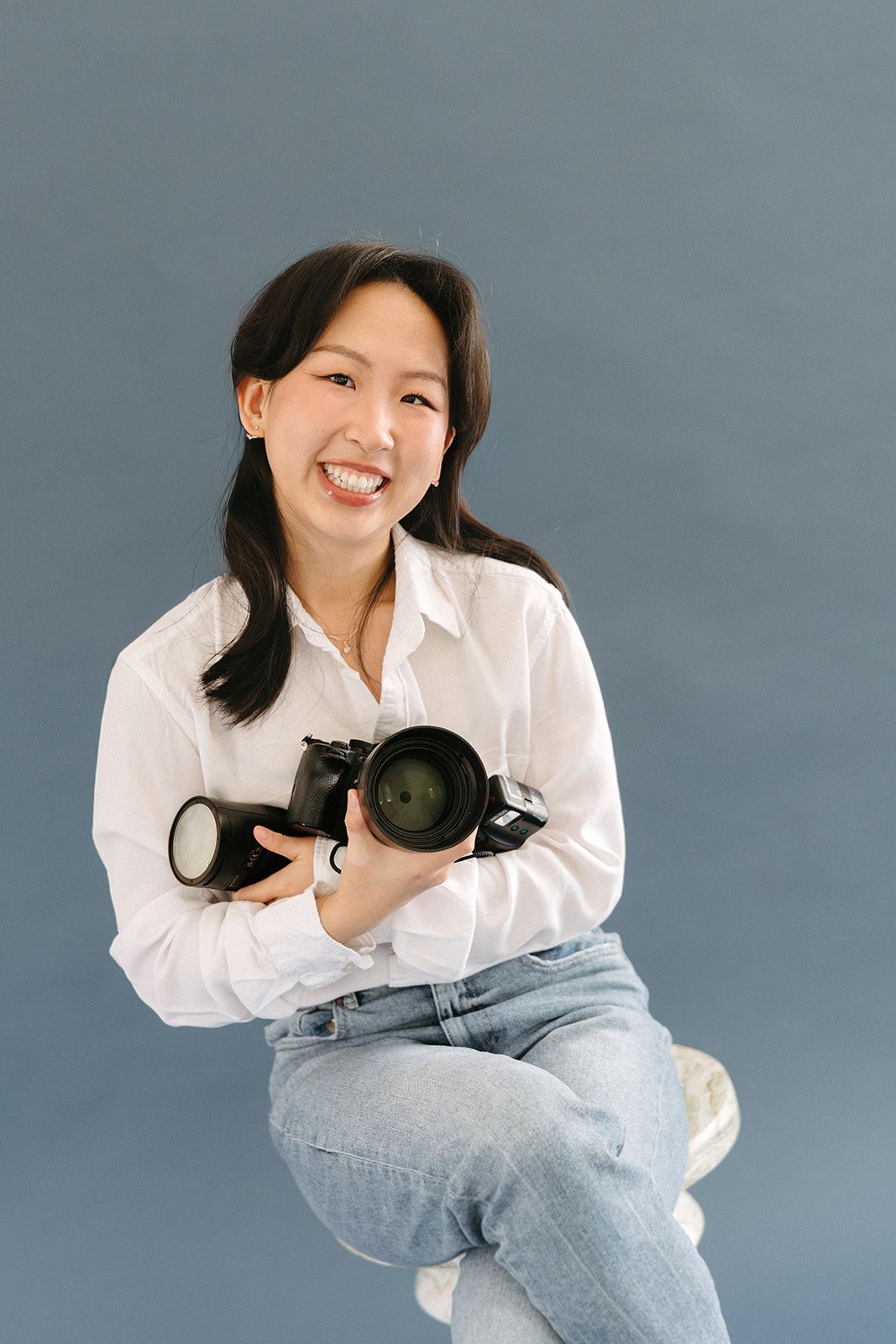 Photographer in white shirt and jeans poses with camera against gray backdrop in four dynamic shots.