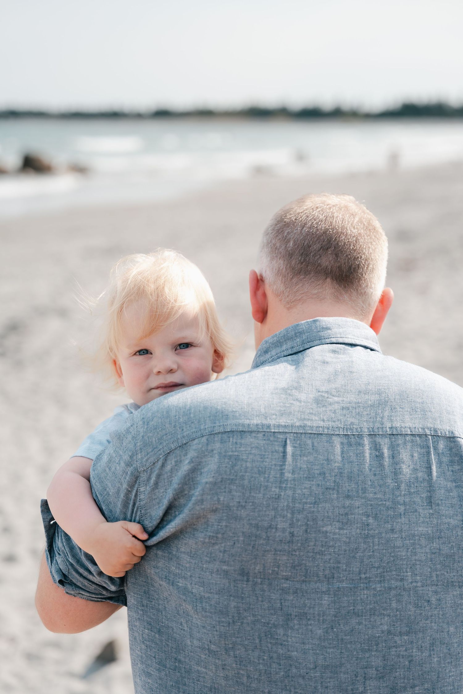 A sequence of photos shows a small child peeking over an adult's shoulder at the beach, creating a playful moment in Halifax, Nova Scotia.