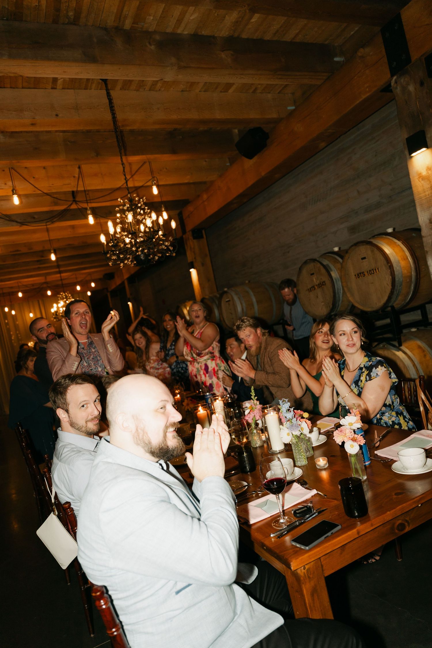 Guests enjoying a lively dinner party in a rustic wine cellar with wooden barrels and hanging lights at Lightfoot & Wolfville.