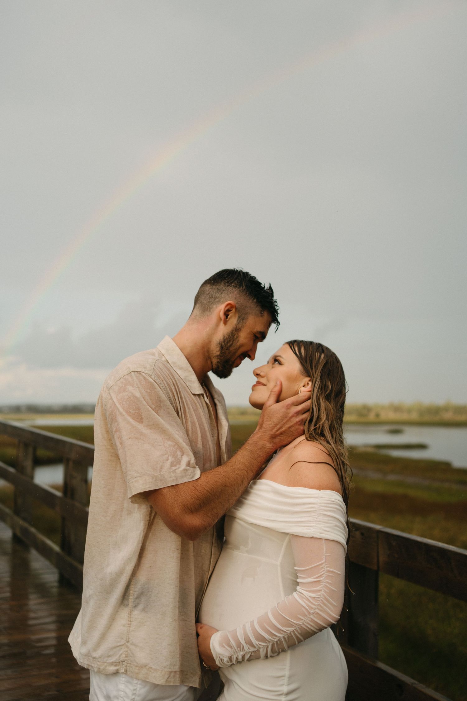 Romantic couple shares intimate moments during sunset photoshoot on wooden boardwalk near coastal marsh in Halifax, Nova Scotia.