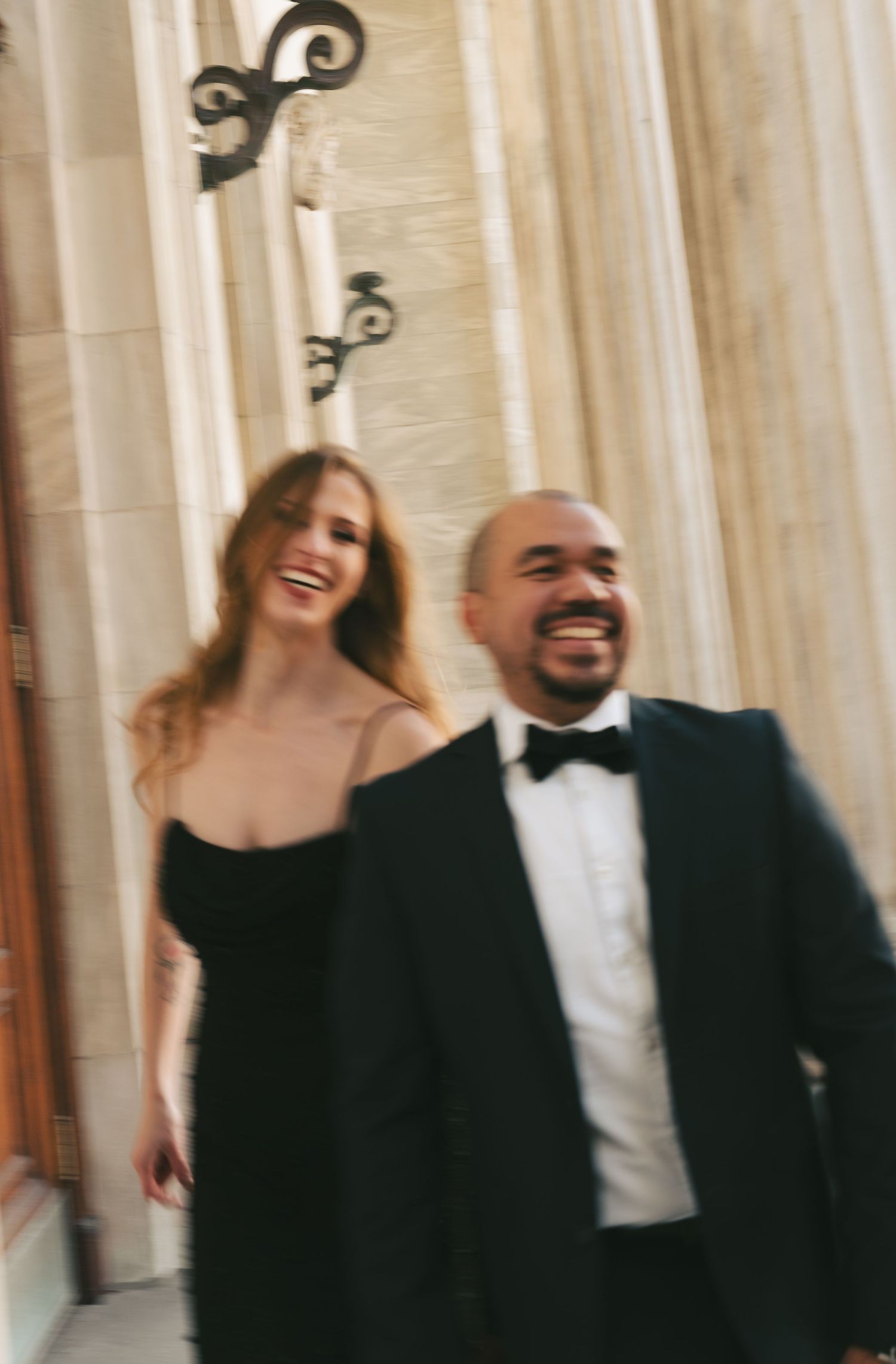 Couple in formal attire laughing and dancing together in an elegant venue in Montreal, Quebec with white pillars.
