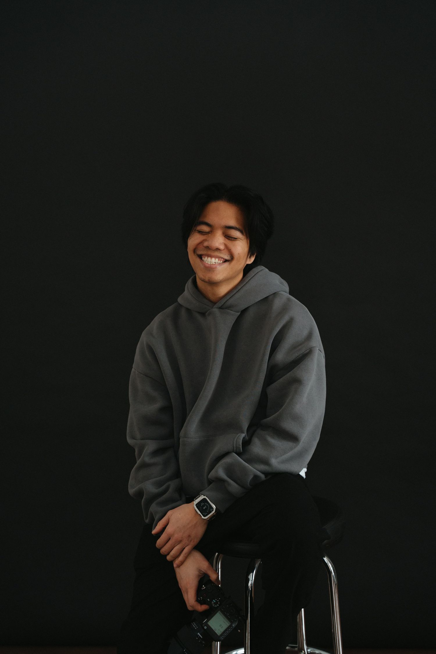 Person wearing a grey hoodie smiles and poses against dark background in a sequence of candid shots in Halifax, Nova Scotia.