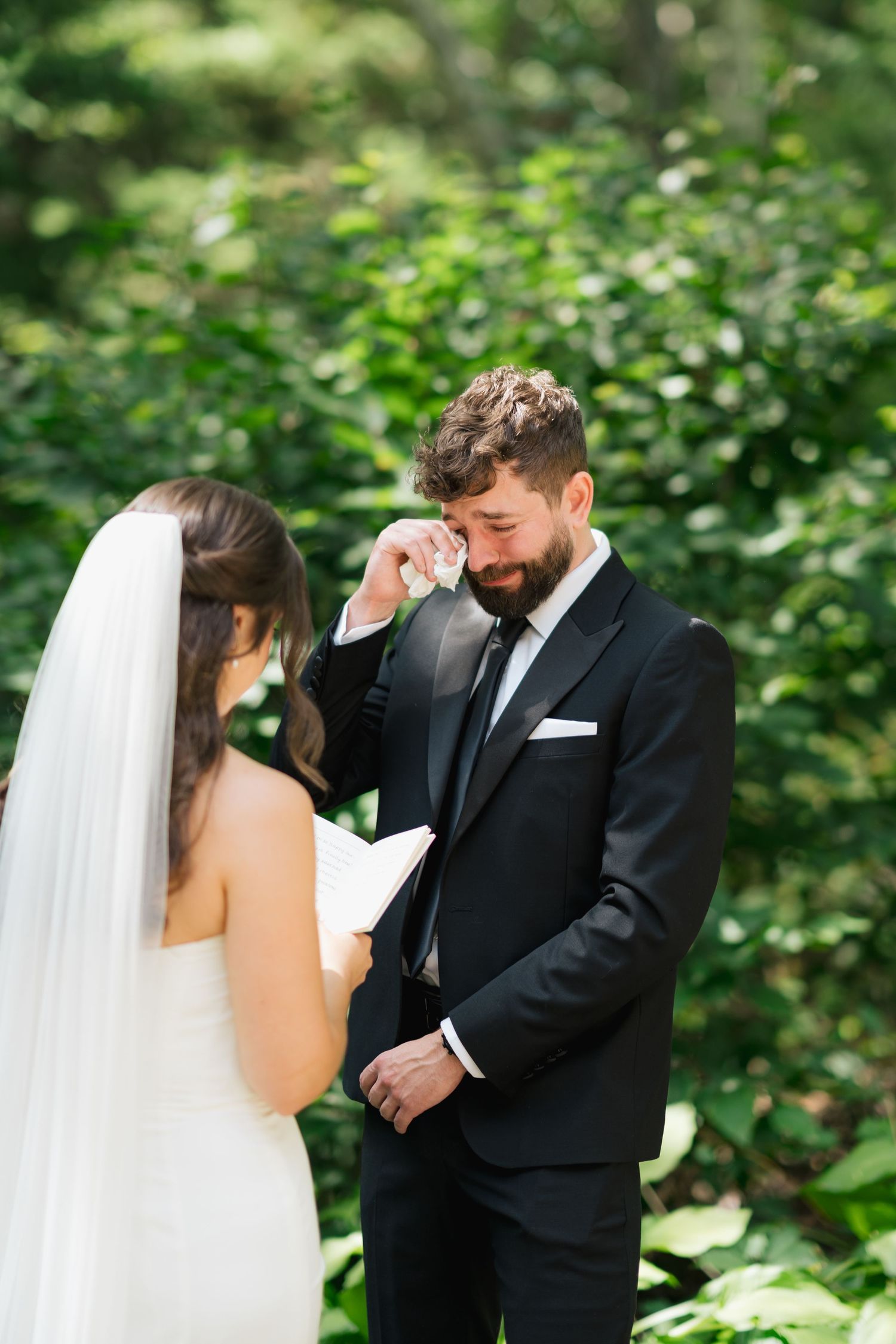 An emotional wedding ceremony moment between a couple surrounded by lush greenery during their outdoor vows in Halifax, Nova Scotia.