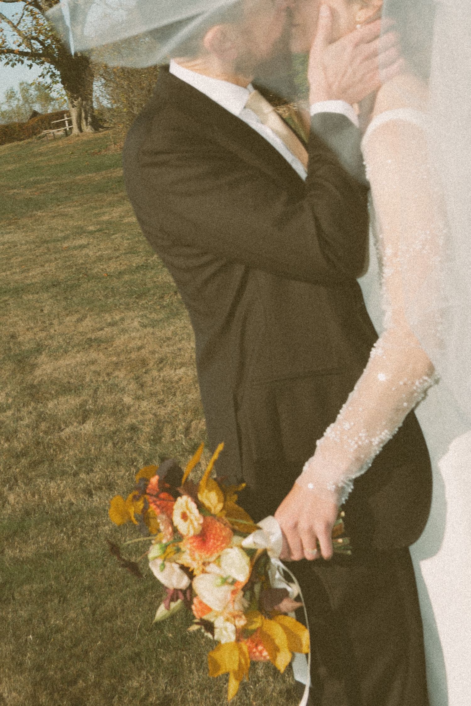 A couple embraces on their wedding day with the bride holding a vibrant fall-colored bouquet against a grassy outdoor setting in Halifax.