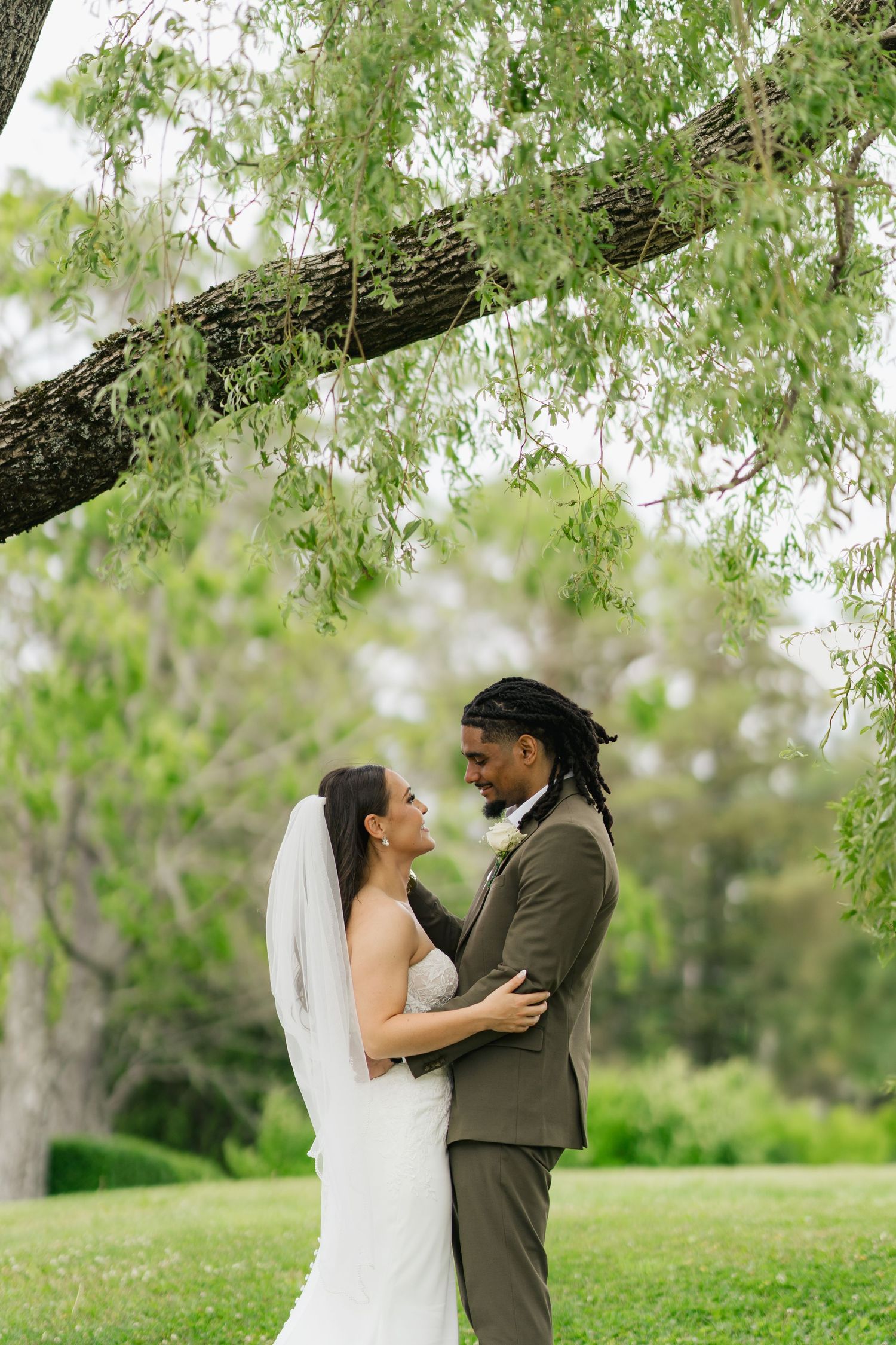 A romantic couple shares an intimate moment under blooming trees in a lush spring garden setting in Halifax, Nova Scotia.