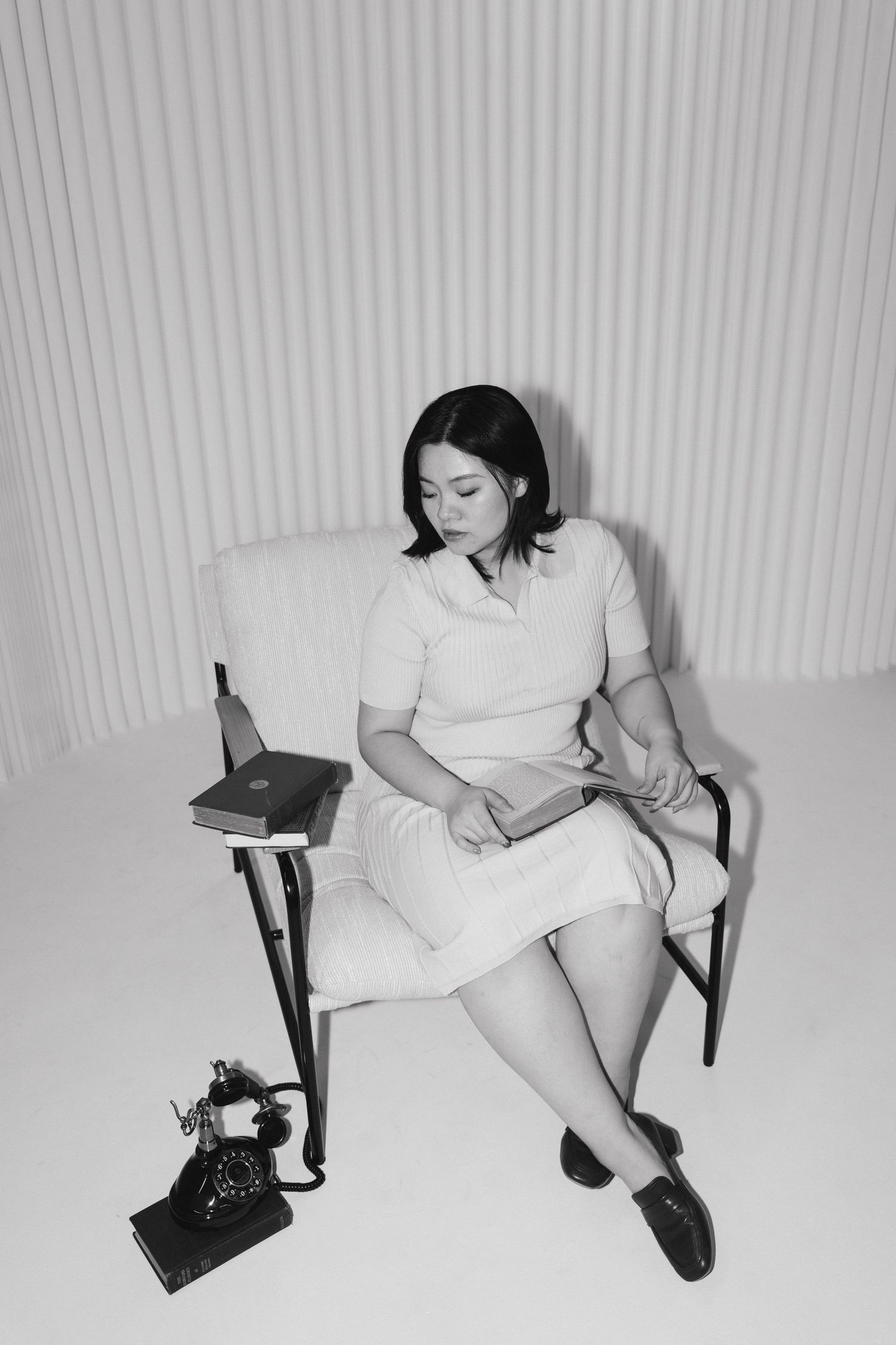 A black and white photo series showing someone in white clothing reclining on a chair against a striped wall background in Halifax, NS.