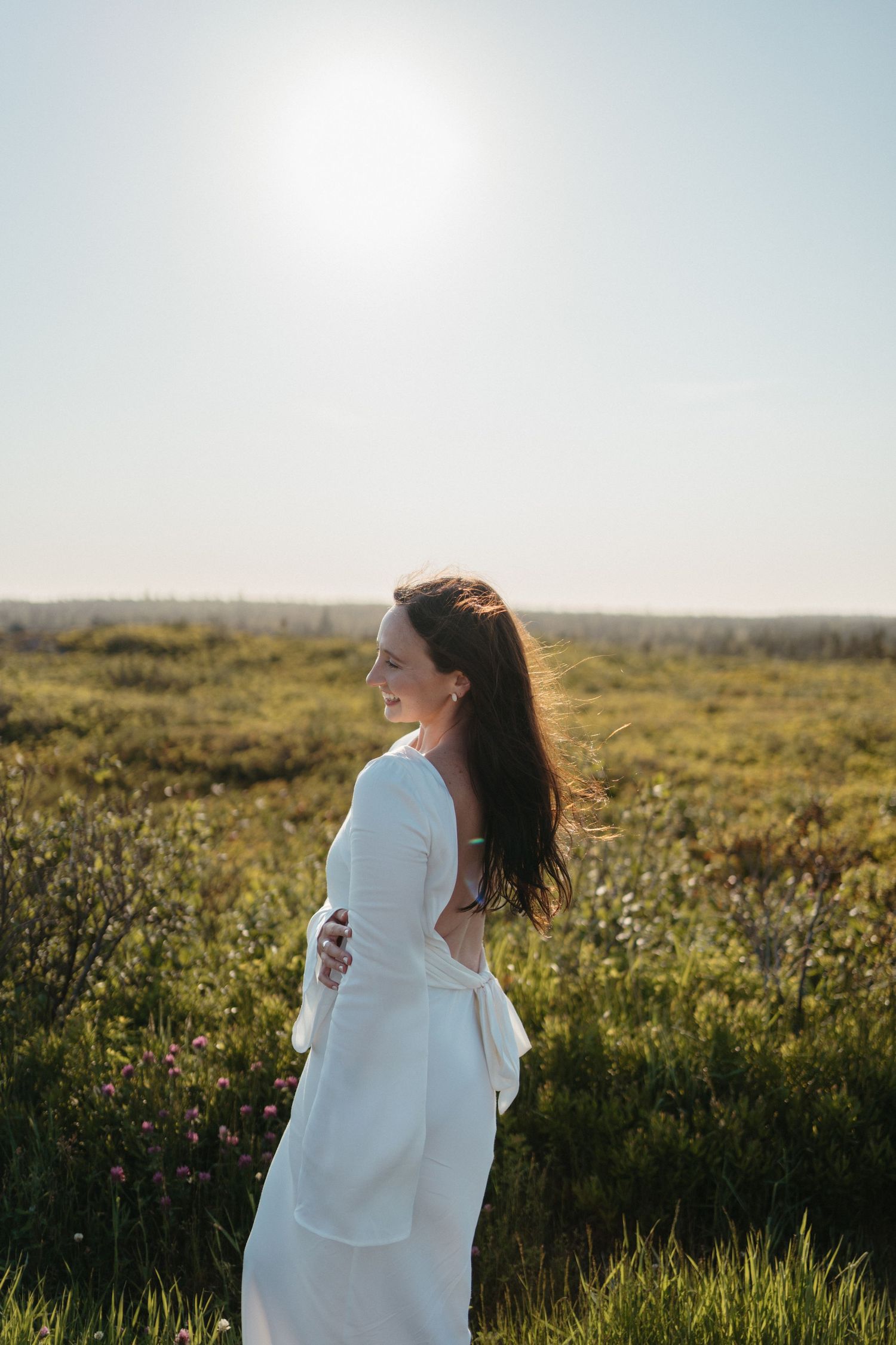 A person in a flowing white dress spins joyfully in a sunlit meadow filled with wildflowers at golden hour in Halifax, Nova Scotia.