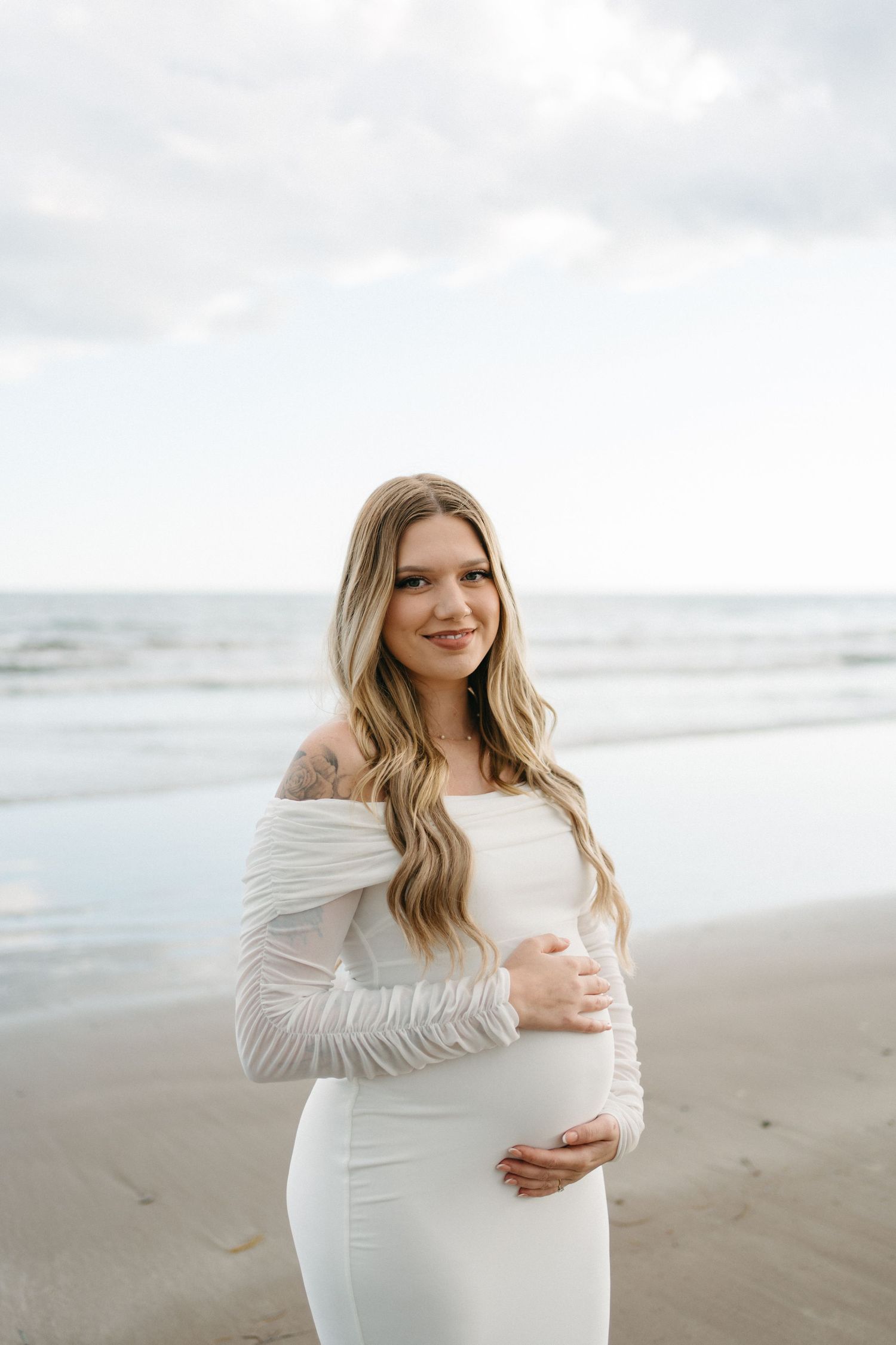 Expectant mother in flowing white dress poses joyfully on a misty beach during maternity photoshoot in Halifax, Nova Scotia.