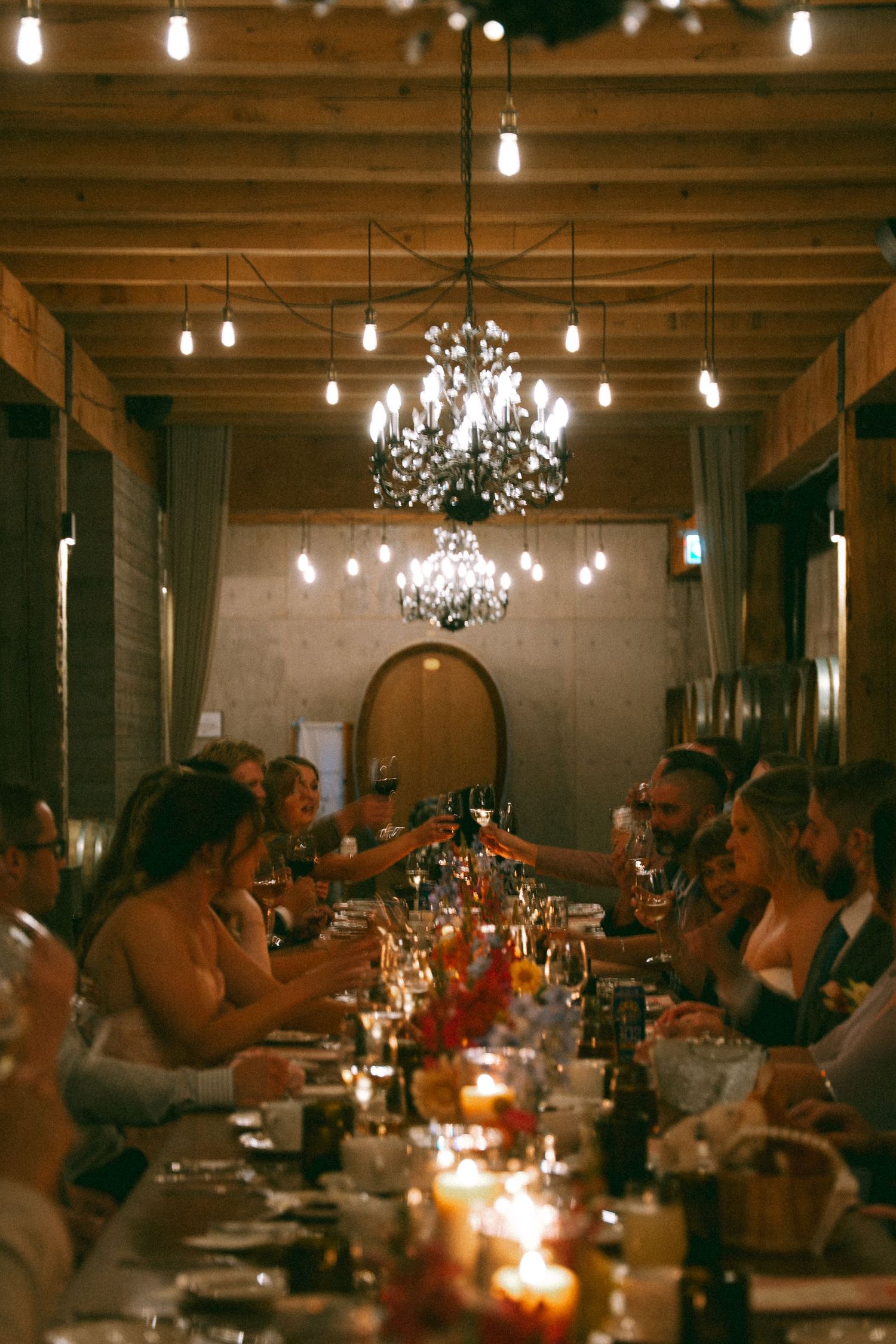 Intimate dinner gathering in a wine cellar with candlelight, chandeliers, and large wooden barrels lining the walls at Lightfoot & Wolfville