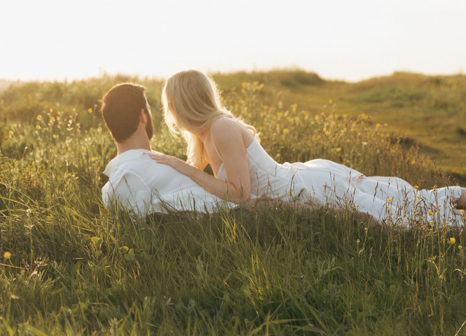 A couple lies together in tall grass during golden hour sunset in Halifax, Nova Scotia.