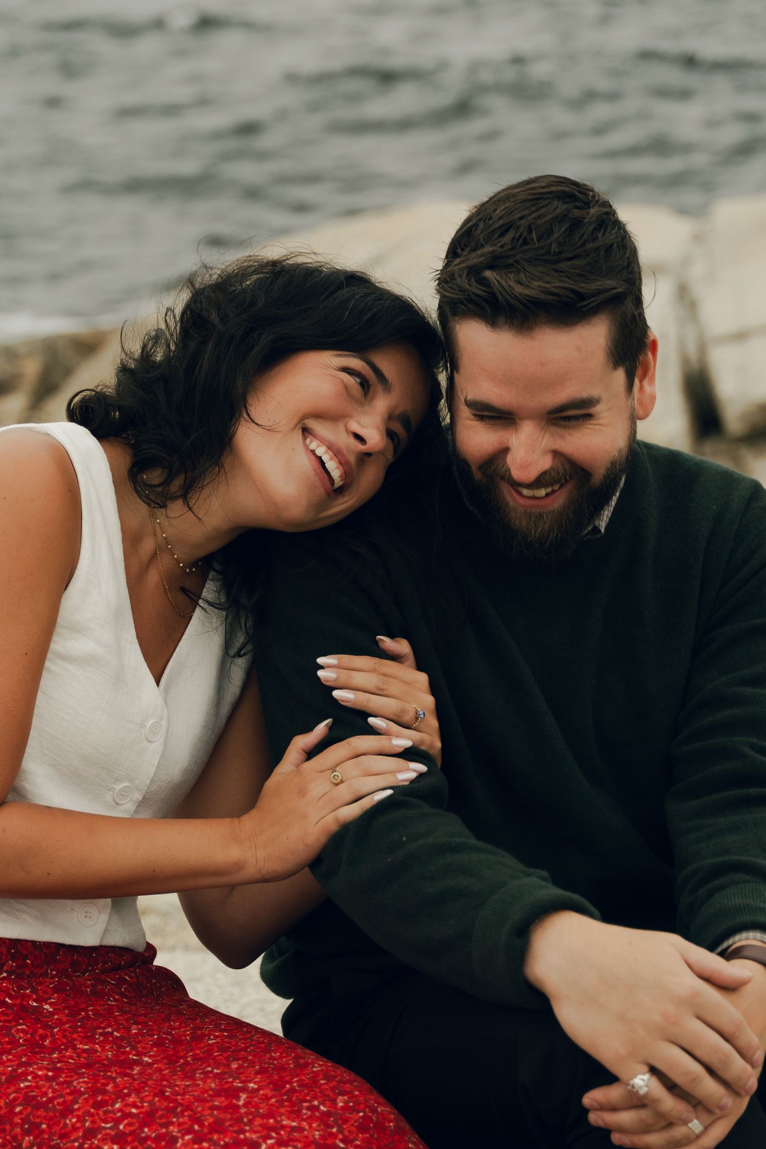 A couple laughs together while sharing a romantic moment on a rocky beach in Halifax, Nova Scotia.