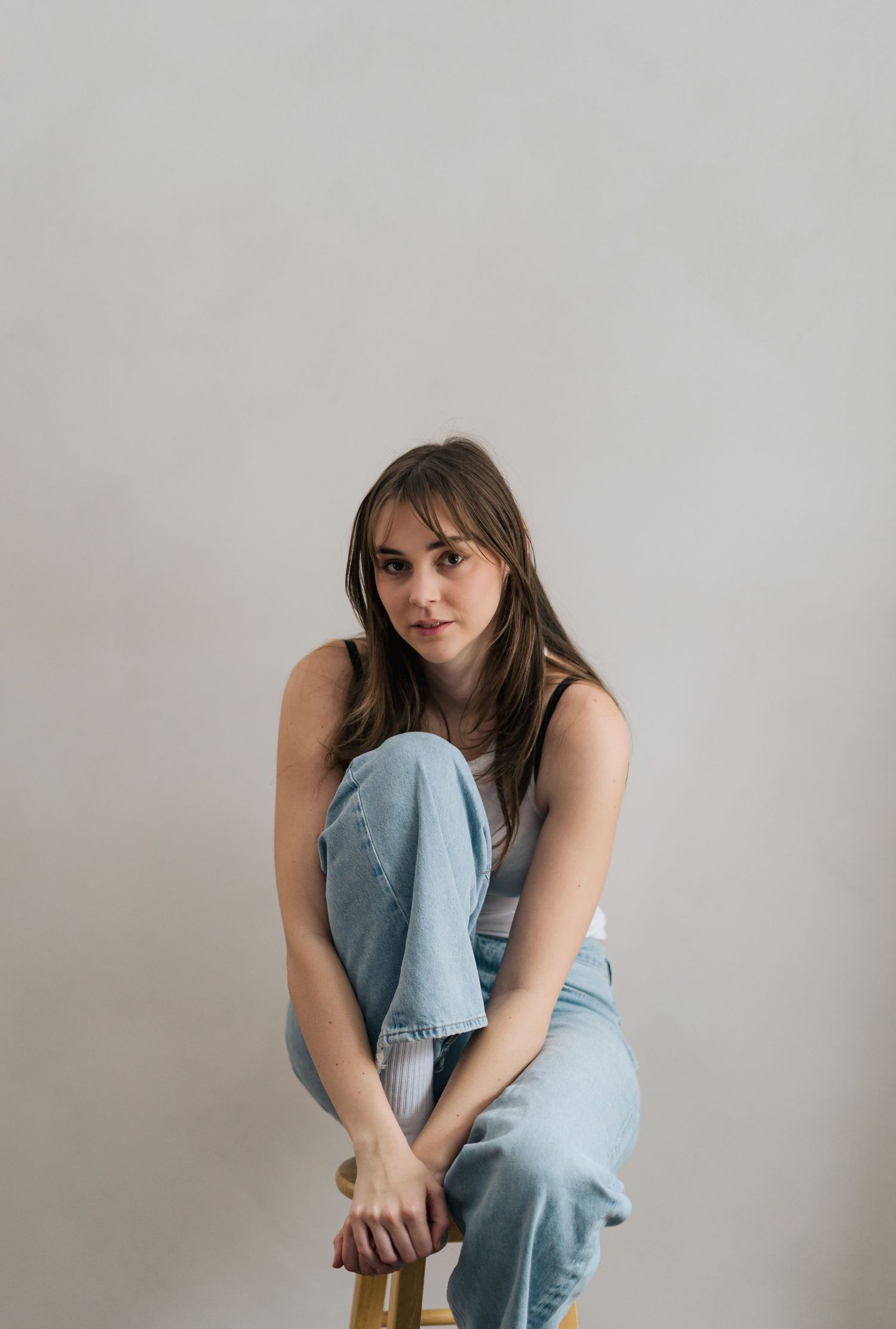 A series of casual poses on a wooden chair against a white background wearing denim and a dark top in Halifax, Nova Scotia.