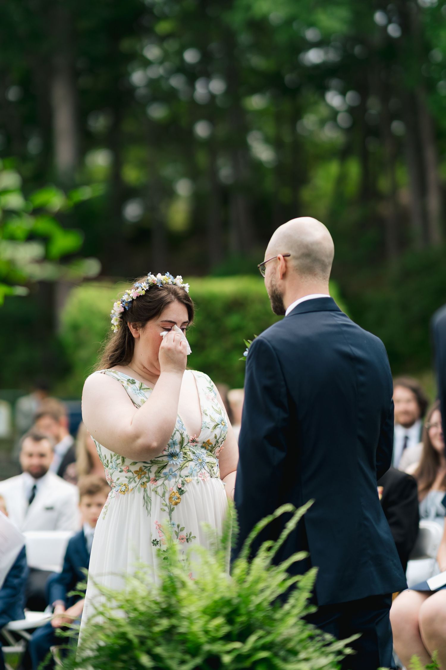 A couple exchanges vows during an outdoor wedding ceremony surrounded by lush greenery and seated guests in Halifax, Nova Scotia.