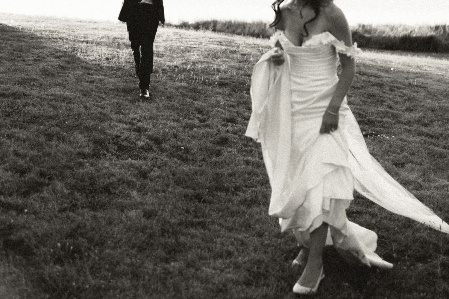 Black and white photo series showing a couple running playfully through a grassy field in wedding attire in Halifax, Nova Scotia.